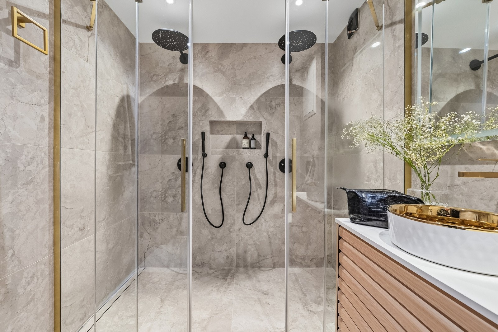 Romslig dusjsone med to takdusjer, elegante glassvegger og detaljer i varme metalltoner. Badet har elektrisk gulvvarme og fremstår som et påkostet og komfortabelt velværeområde. Galleribilde