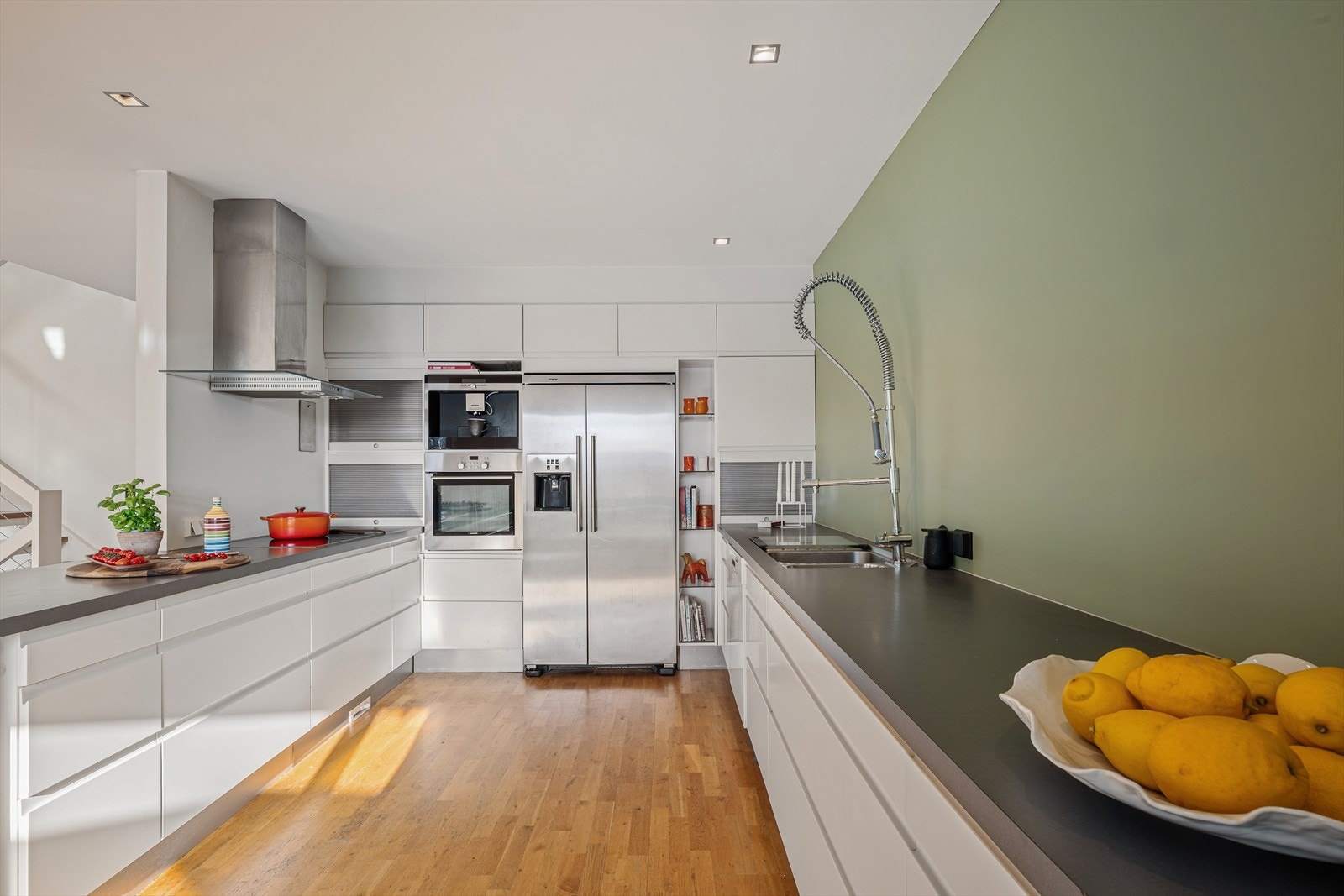 Moderne kjøkkeninnredning med hvitevarer som kjøl/fryseskap, oppvaskmaskin, kaffemaskin, komfyr og platetopp. Galleribilde