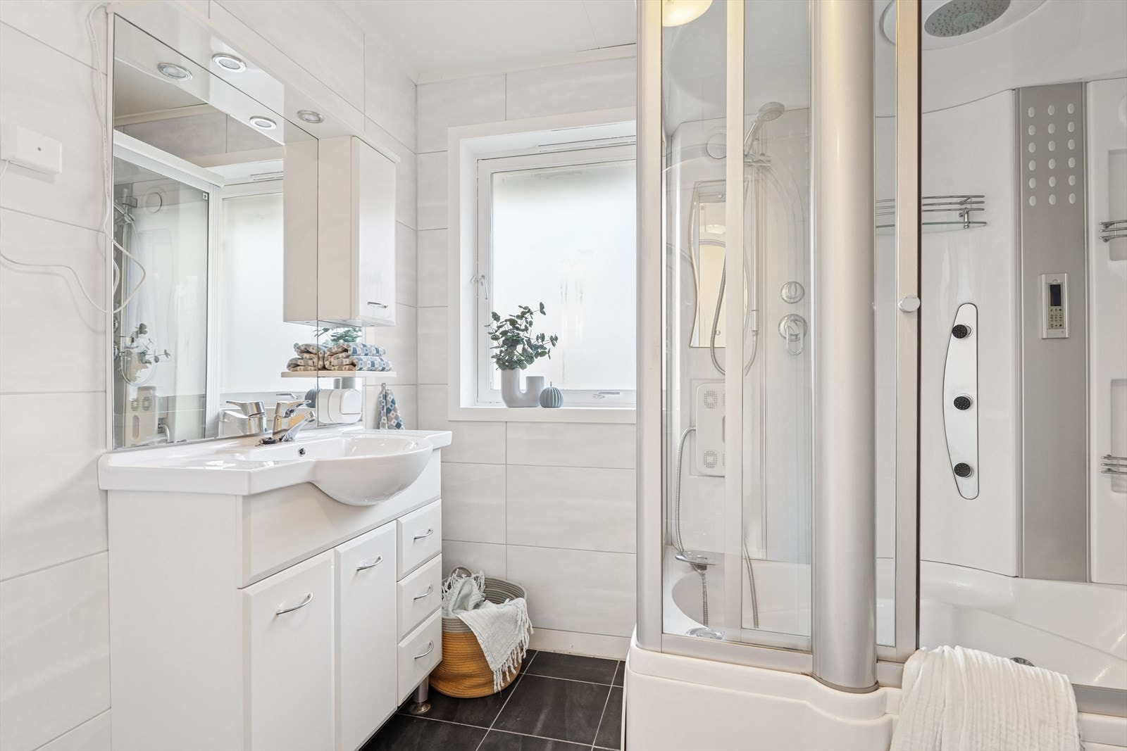 Bad 1: Eldre dusjbad innredet med et stort dusjkabinett med badesokkel og dyser, en servant med skapinnredning og et toalett. Galleribilde