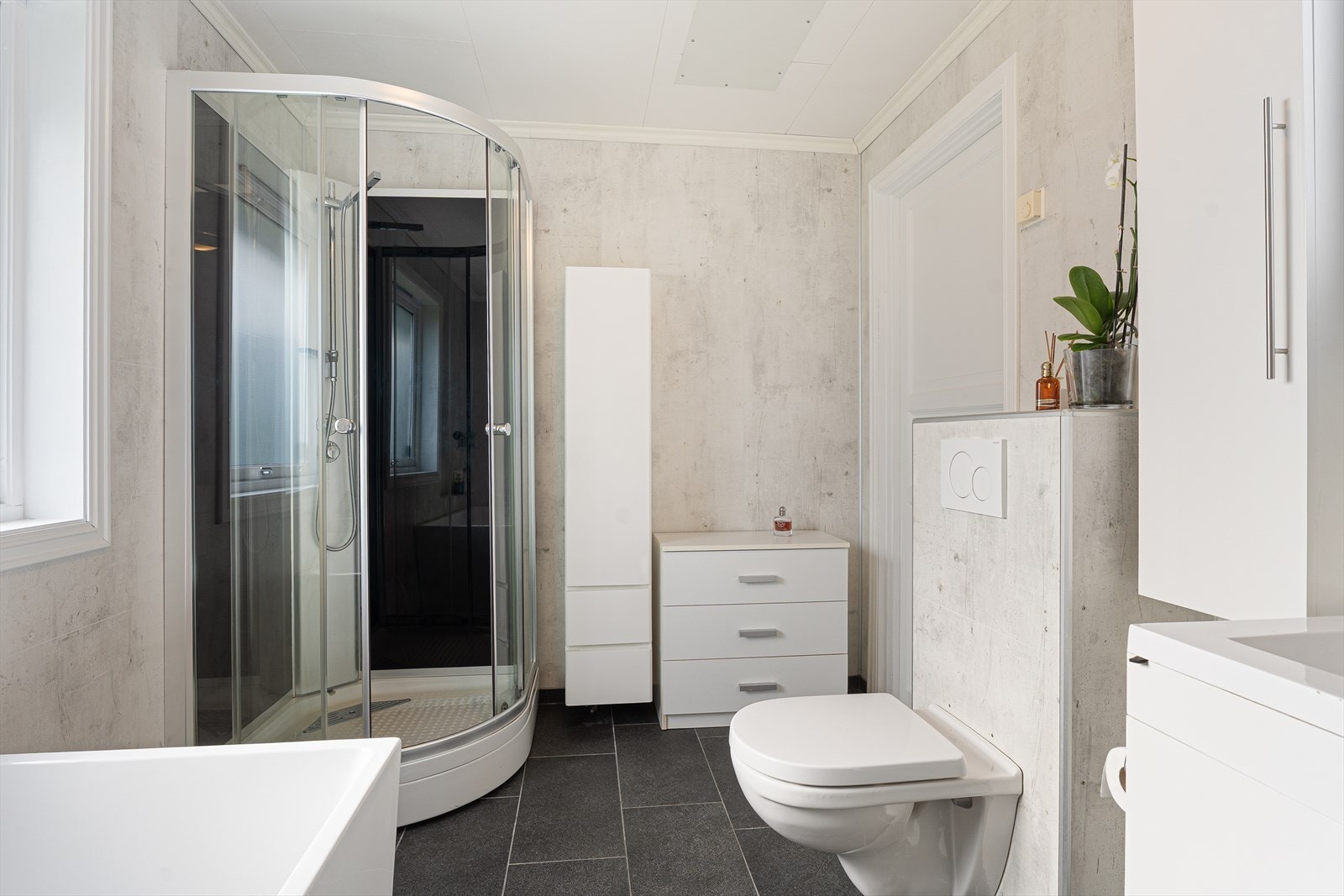 Badet er innredet med speilskap, baderomsinnredning, badekar, dusjkabinett og veggmontert toalett Galleribilde