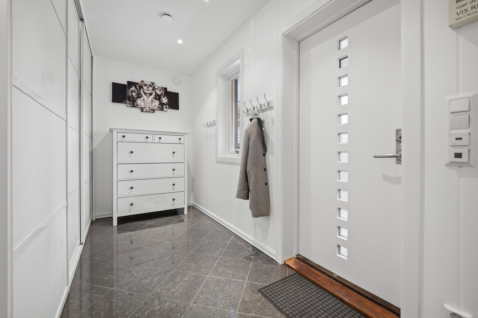 Boligen har en pen entré med hvitmalt panel på veggene, downlights i himlingen og grå fliser på gulv med gulvvarme. Galleribilde