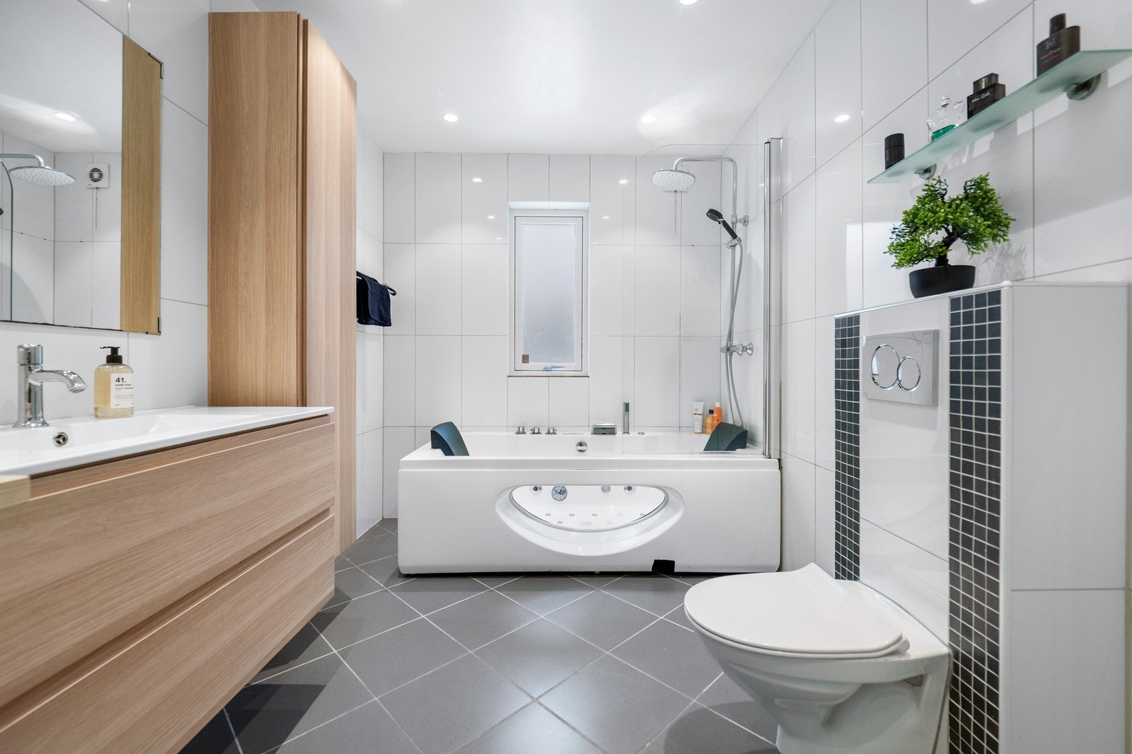 Badet har hvite fliser på veggene, downlights i himlingen og grå fliser på gulv med gulvvarme. Galleribilde