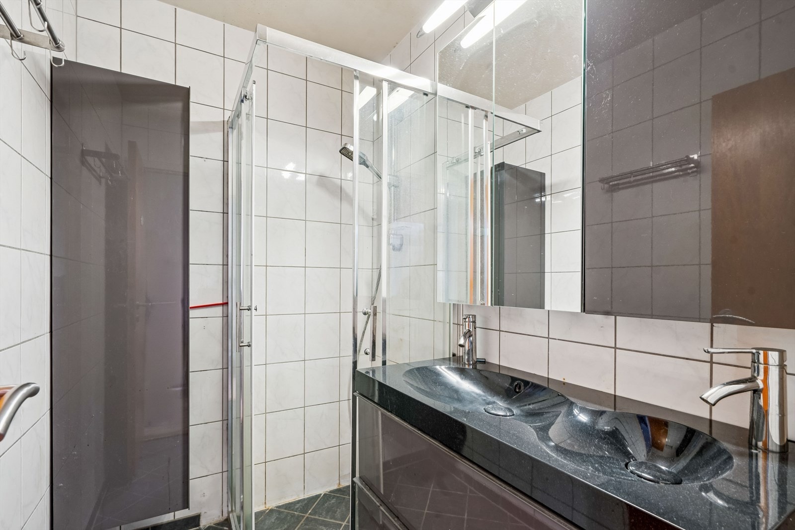 Badet har keramiske fliser på gulv og vegger, dusjnisje med glassdører og en dobbel servant. Galleribilde