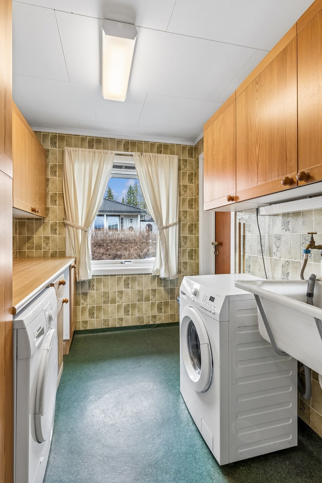 Praktisk vaskerom med utslagsvask, benkeplass og opplegg for vaskemaskin. Galleribilde