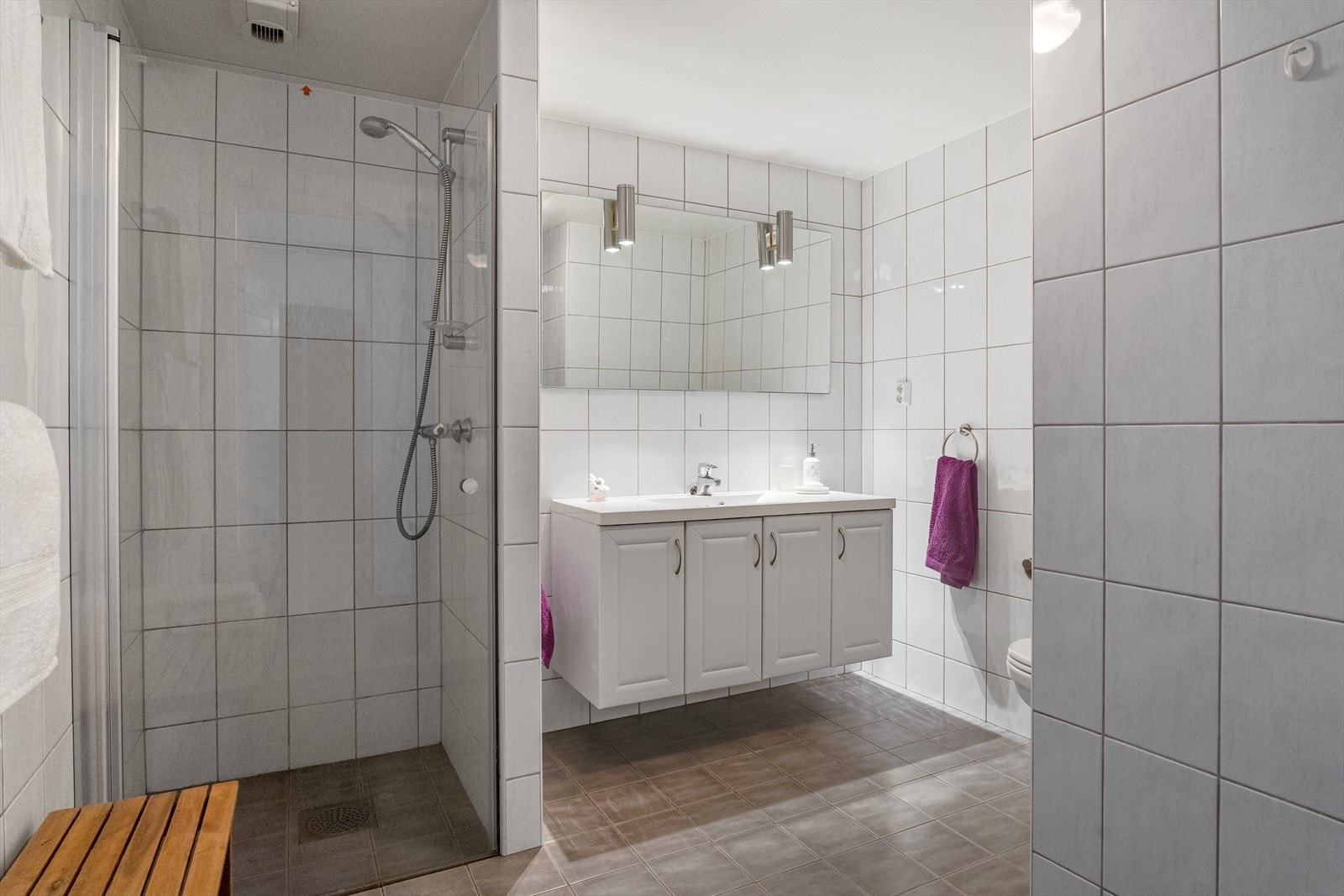 Tiltalende flislagt bad med hvit baderomsinnredning, dusjnisje og wc Galleribilde