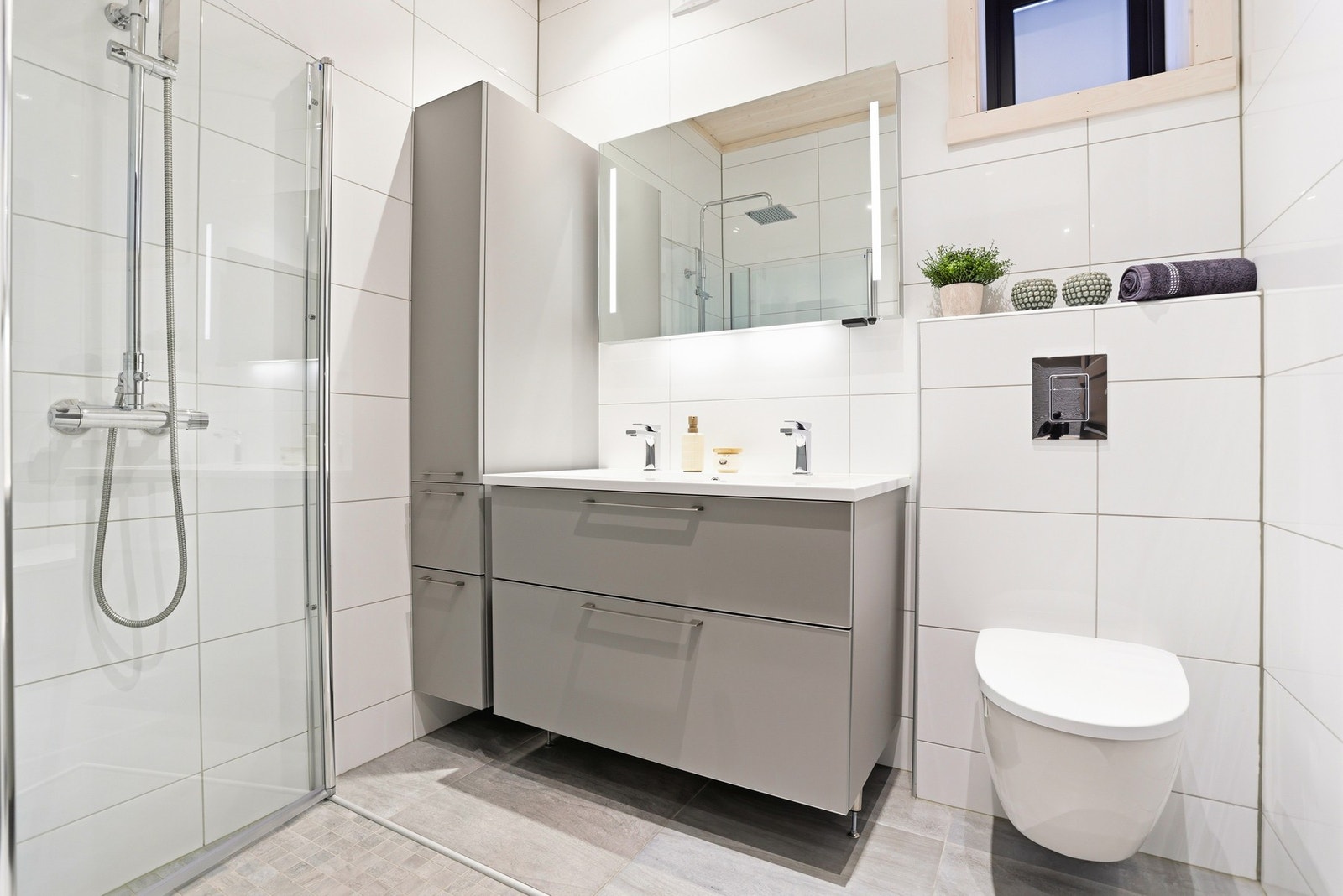 Baderom i 1.etasje ligger ved hovedsoverommet og inneholder vegghengt toalett, innredning med servant og dusjhjørne med glassdører og waterfall-armatur Galleribilde