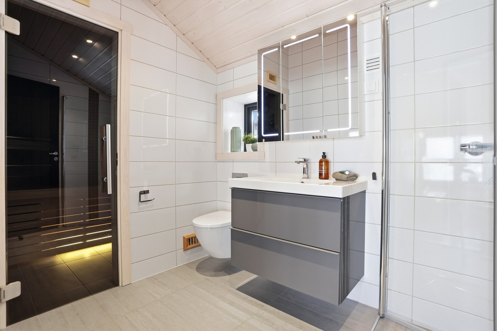 Baderommet i 2.etasje inneholder vegghengt toalett, innredning med servant, dusjhjørne med glassdører og tilgang til badstue Galleribilde