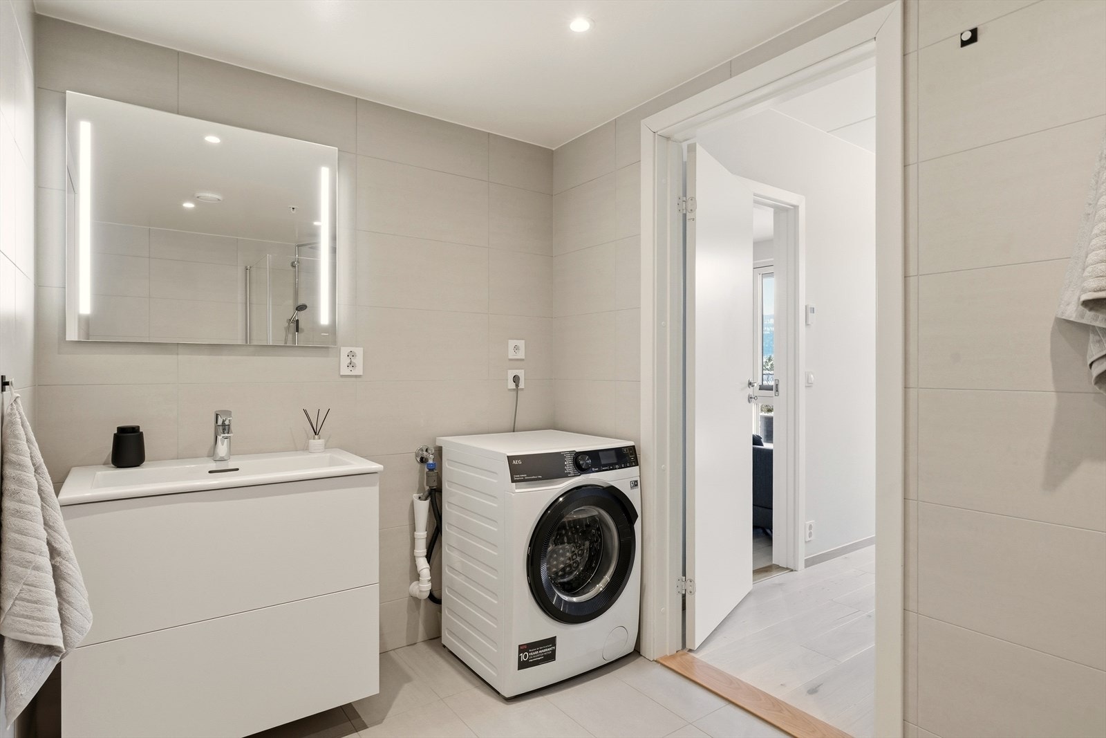 Moderne innredning med skuffer og speil med lys. God plass til vaskemaskin Galleribilde