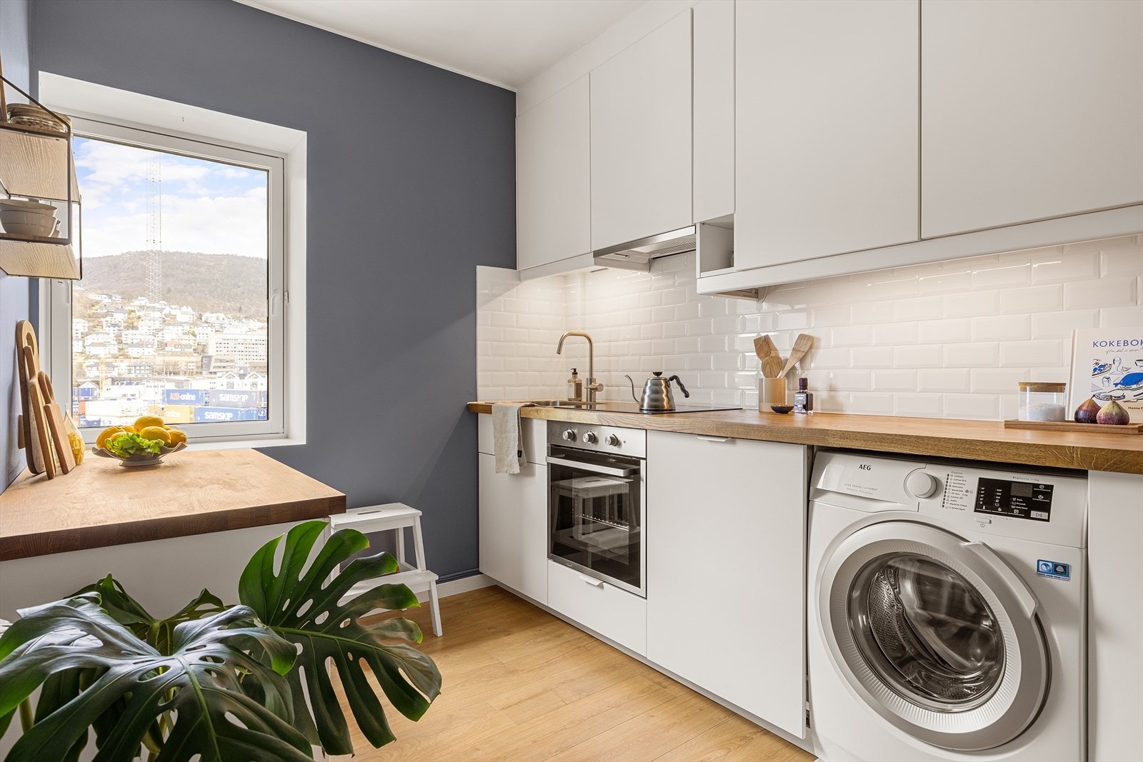 Kjøkkeninnredning med hvite glatte fronter og benkeplate med kjøkkenvask. Galleribilde