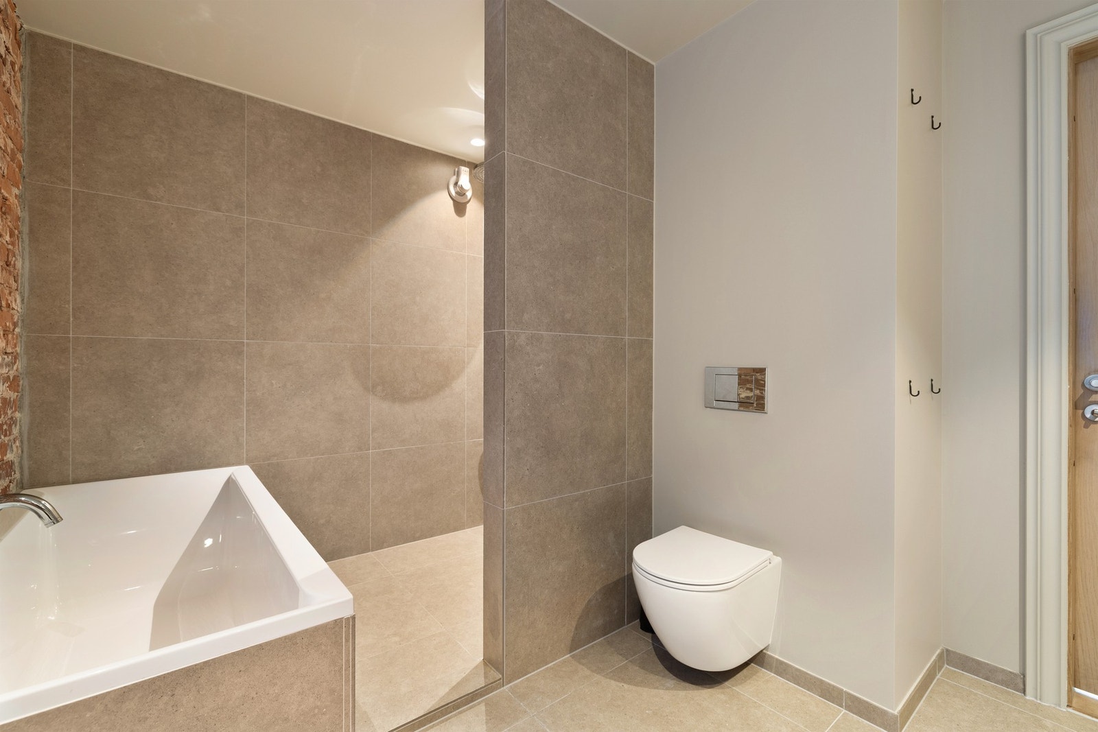 Badet inneholder servant med møblement/betong benk, speil, vegghengt toalett, integrert dusjgarnityr og innfliset badekar. Galleribilde