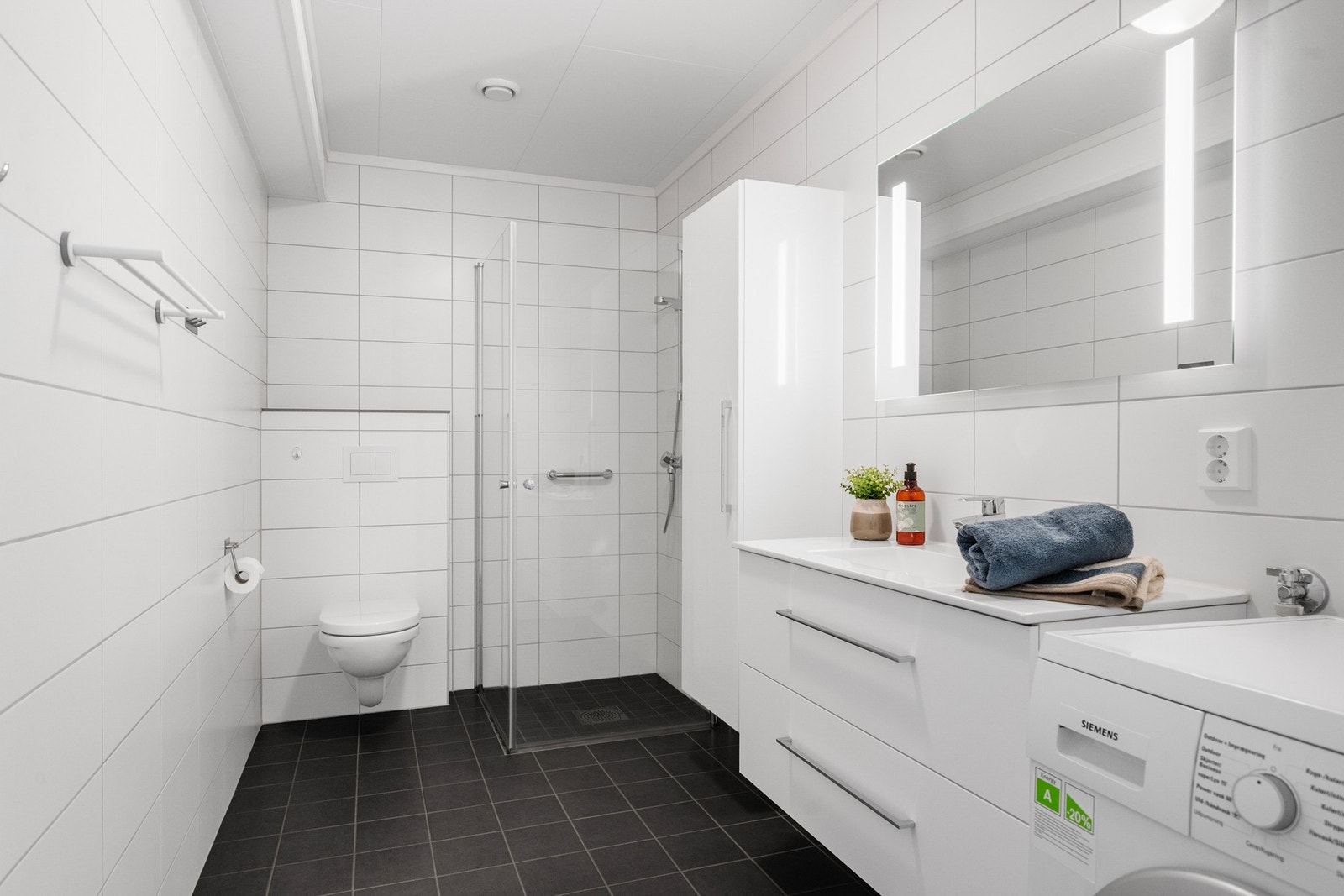 Romslig flislagt bad/wc med dusj, toalett og moderne innredning. Galleribilde