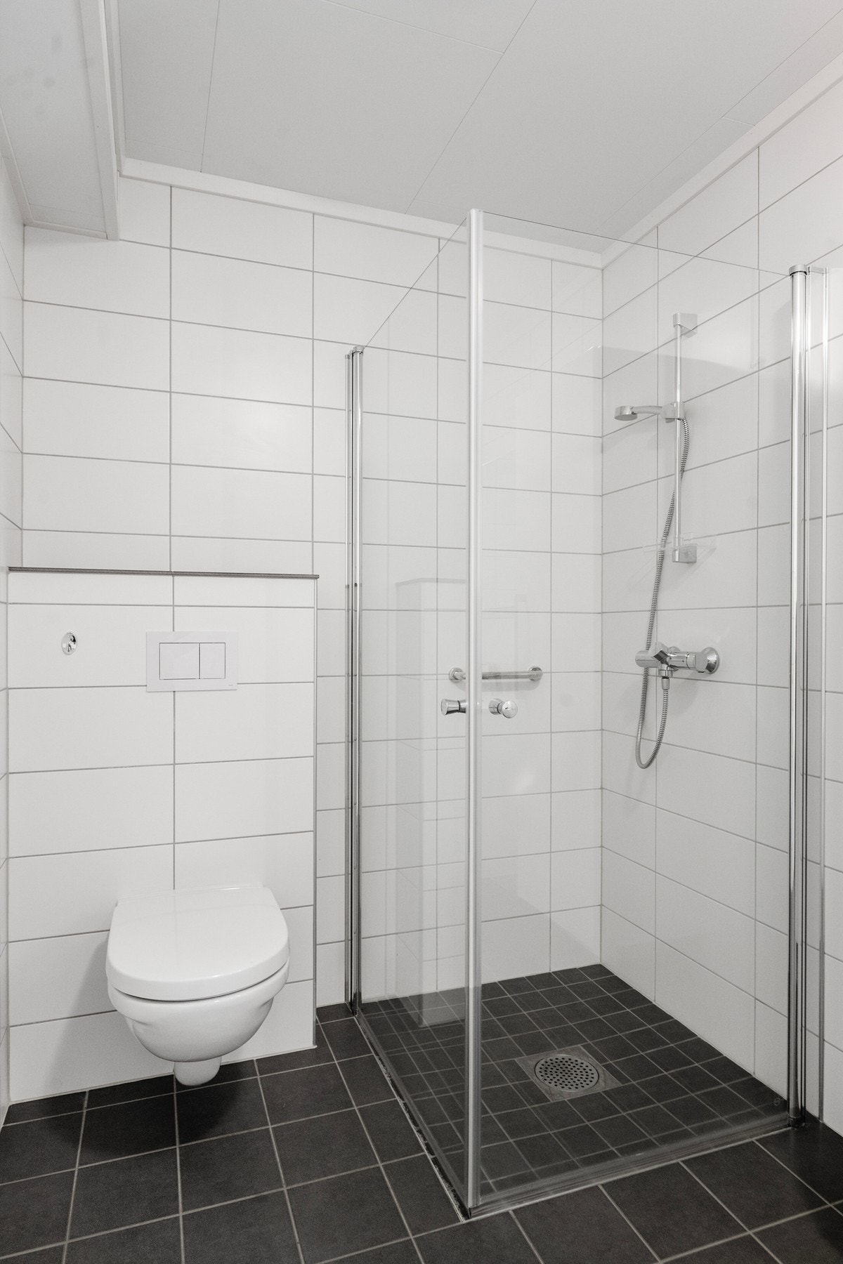 Badet har dusj og vegghengt toalett. Fliser på gulv og vegger. Varme i gulv. Galleribilde