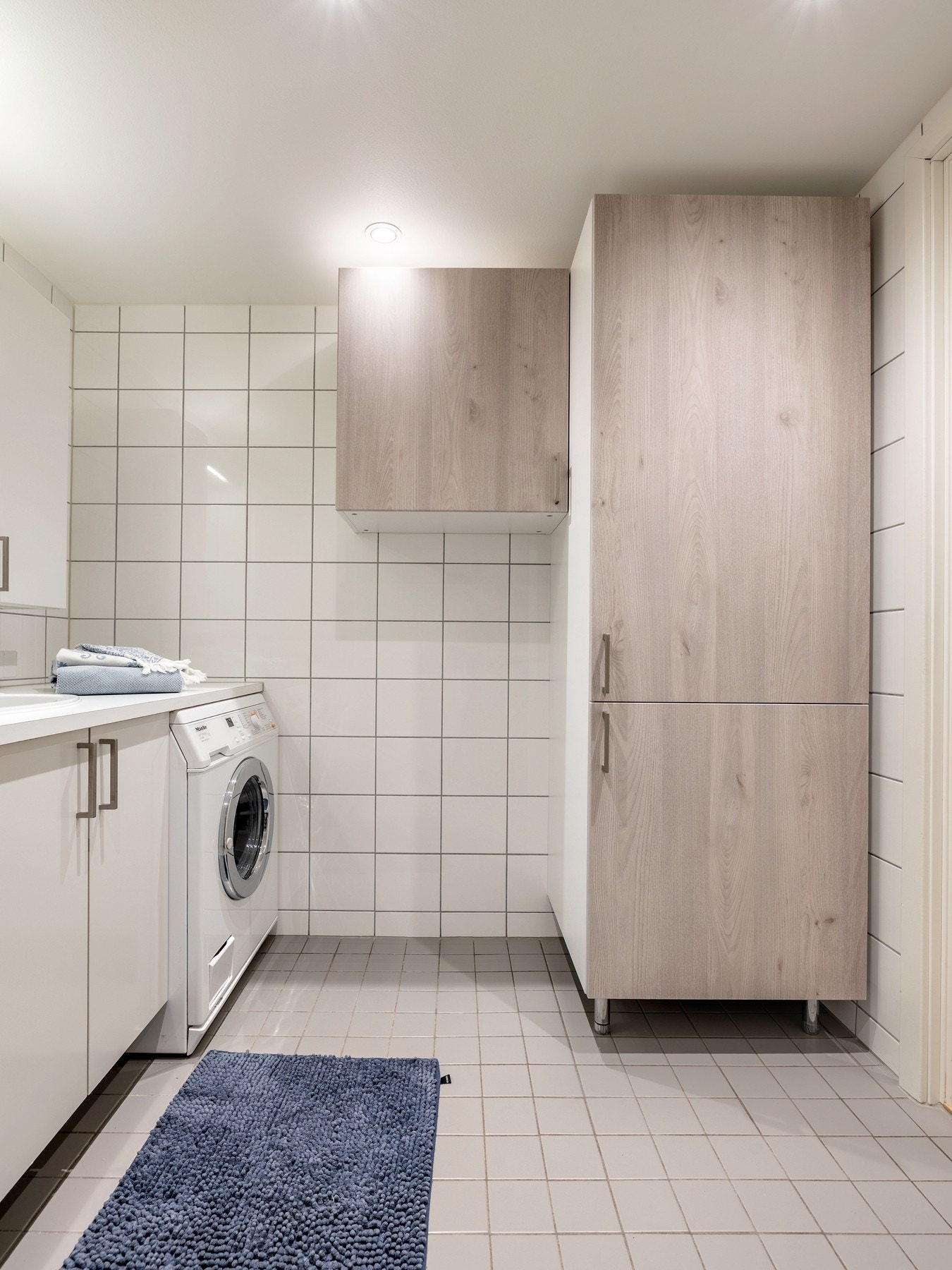 Det er plass for vaskemaskin og tørketrommel under benkeplate, og det er ekstra oppbevaringsplass i høyskap og overskap på den ene veggen. Galleribilde