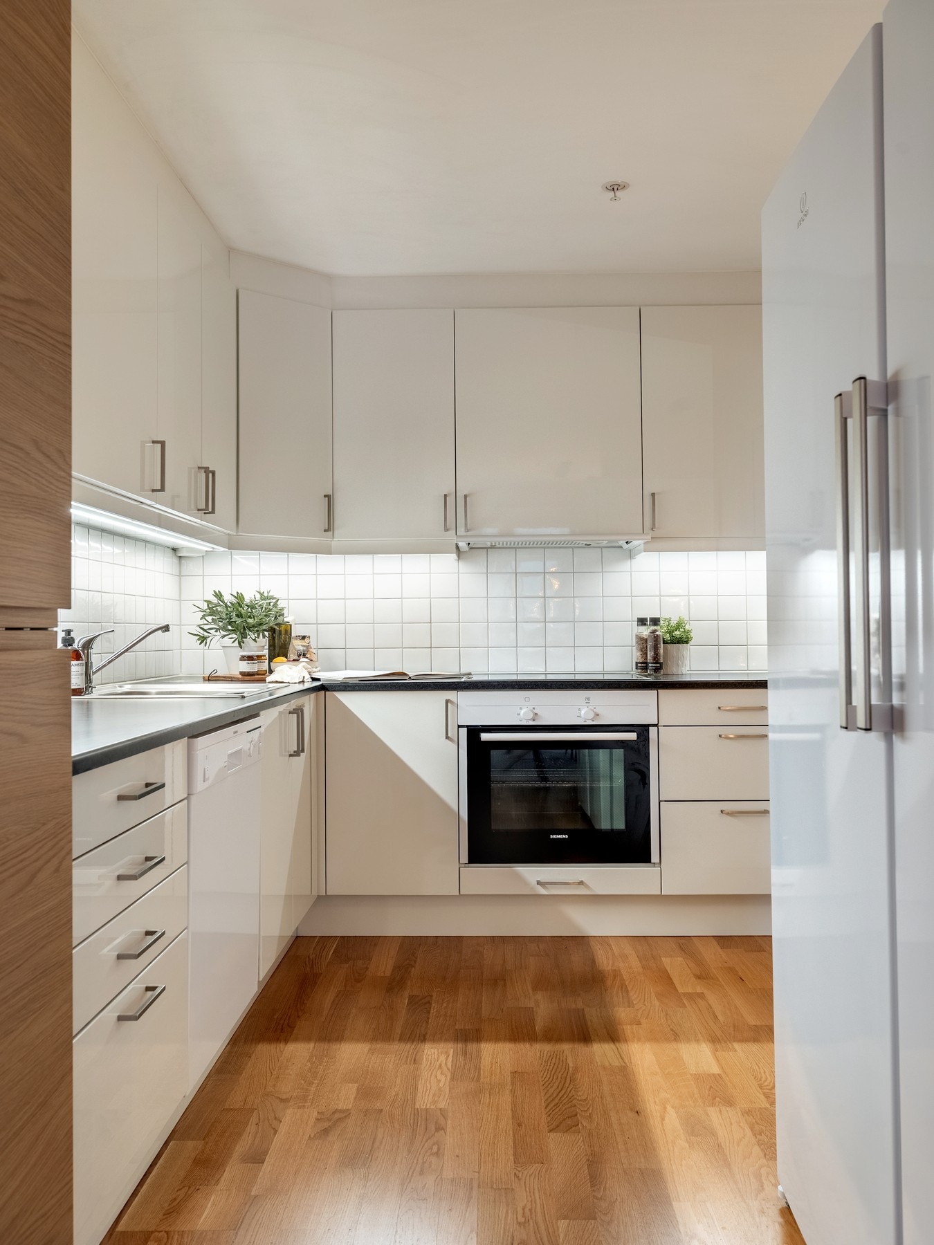 Kjøkkenet har slette fronter i hvit høyglans kombinert med ett høyskap med laminert trefarge. Galleribilde