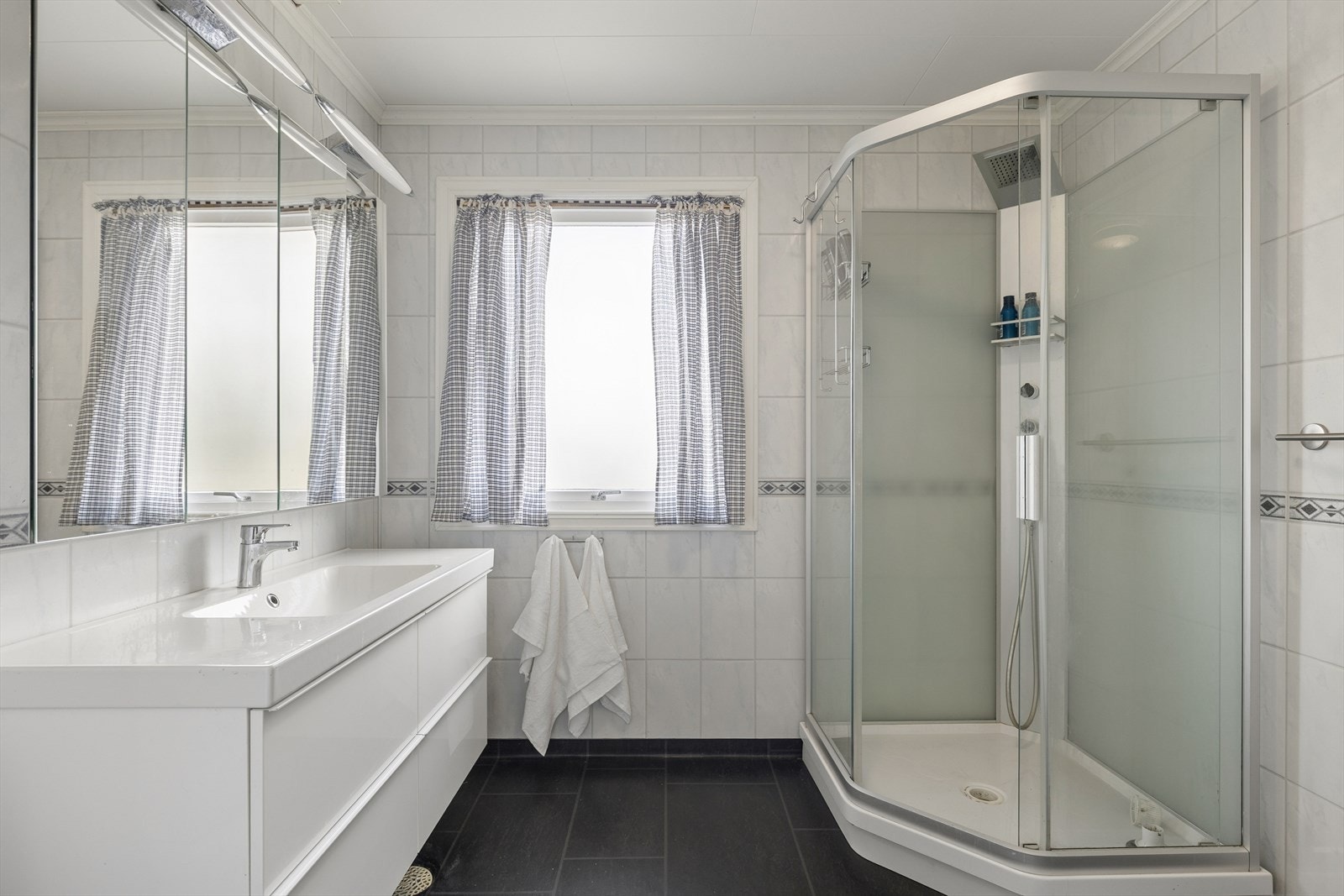 Lyst og innbydende baderom med dusjkabinett, toalett og speil- og servantskap. Galleribilde