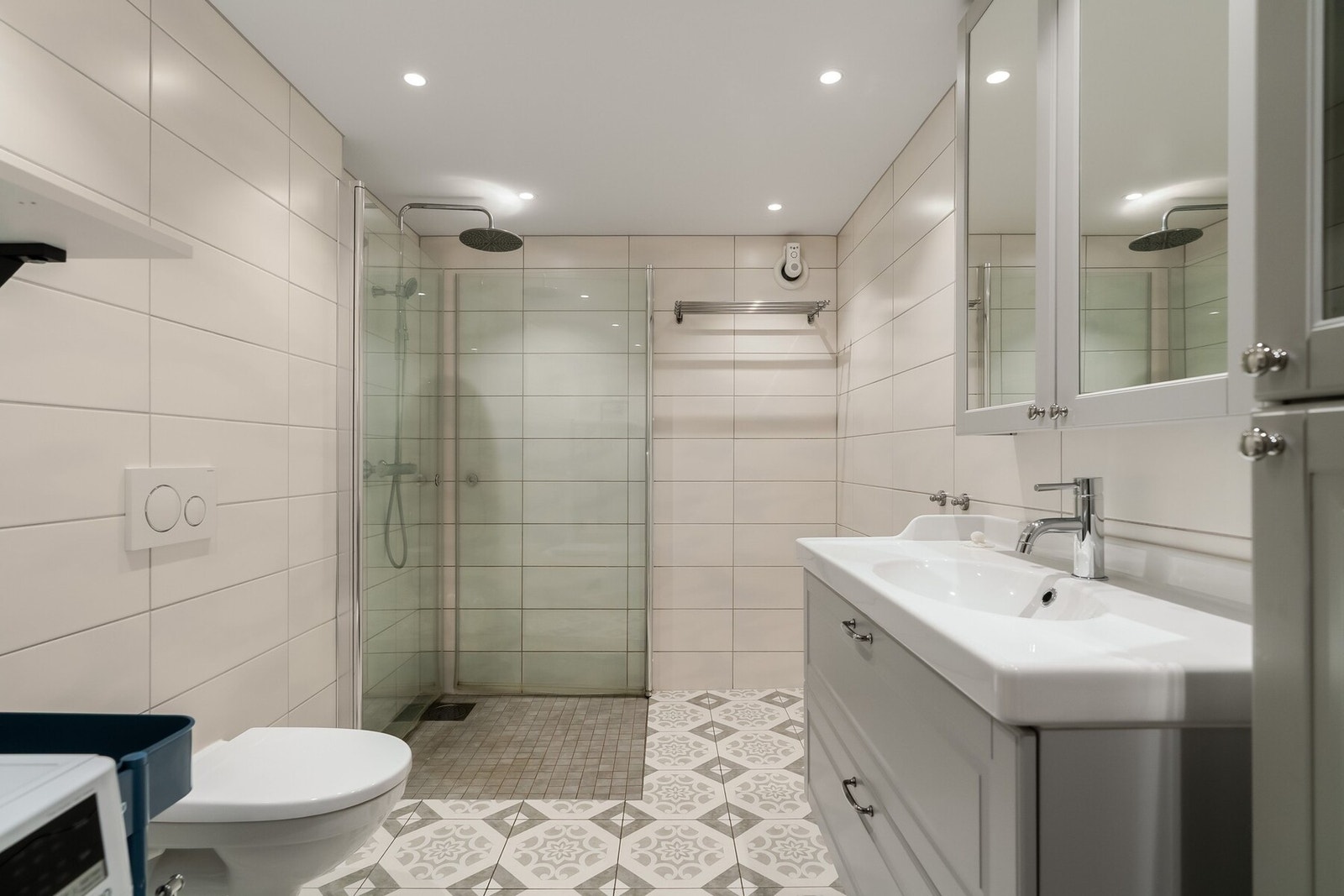 Flislagt bad med regndusj, vegghengt toalett og servant med speilskap. Downlights i taket gir et moderne og behagelig lys. Galleribilde