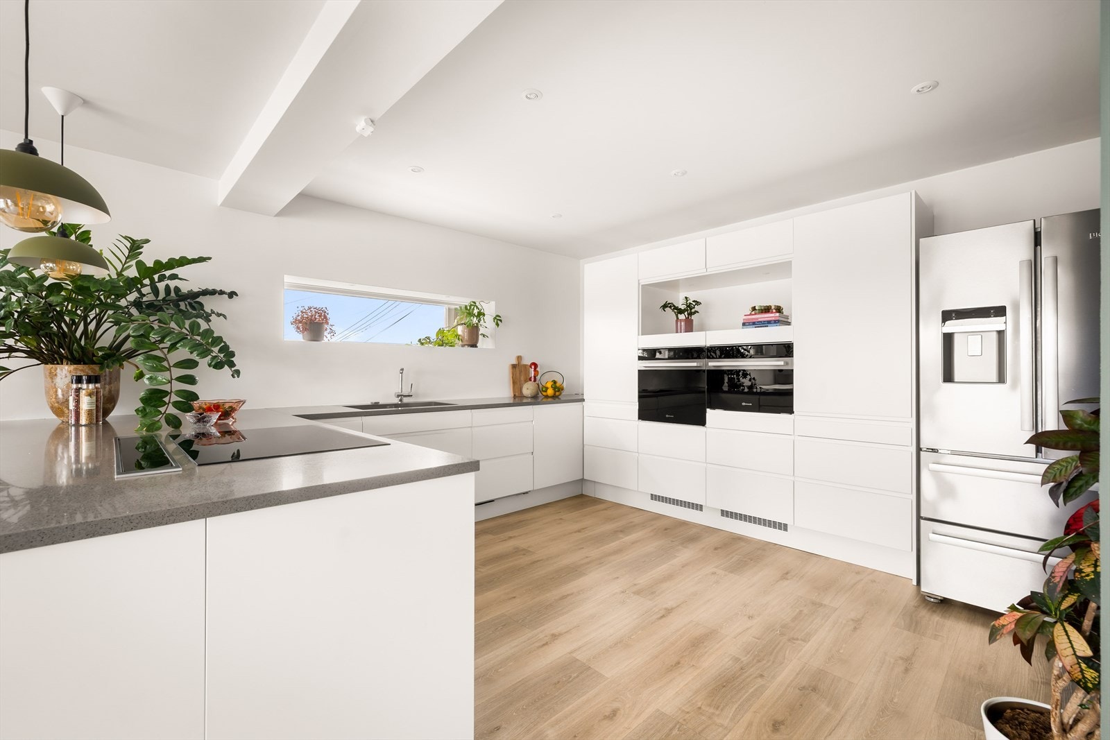 Kjøkkeninnredningen har slette, hvite fronter og integrerte hvitevarer i praktisk arbeidshøyde. Galleribilde