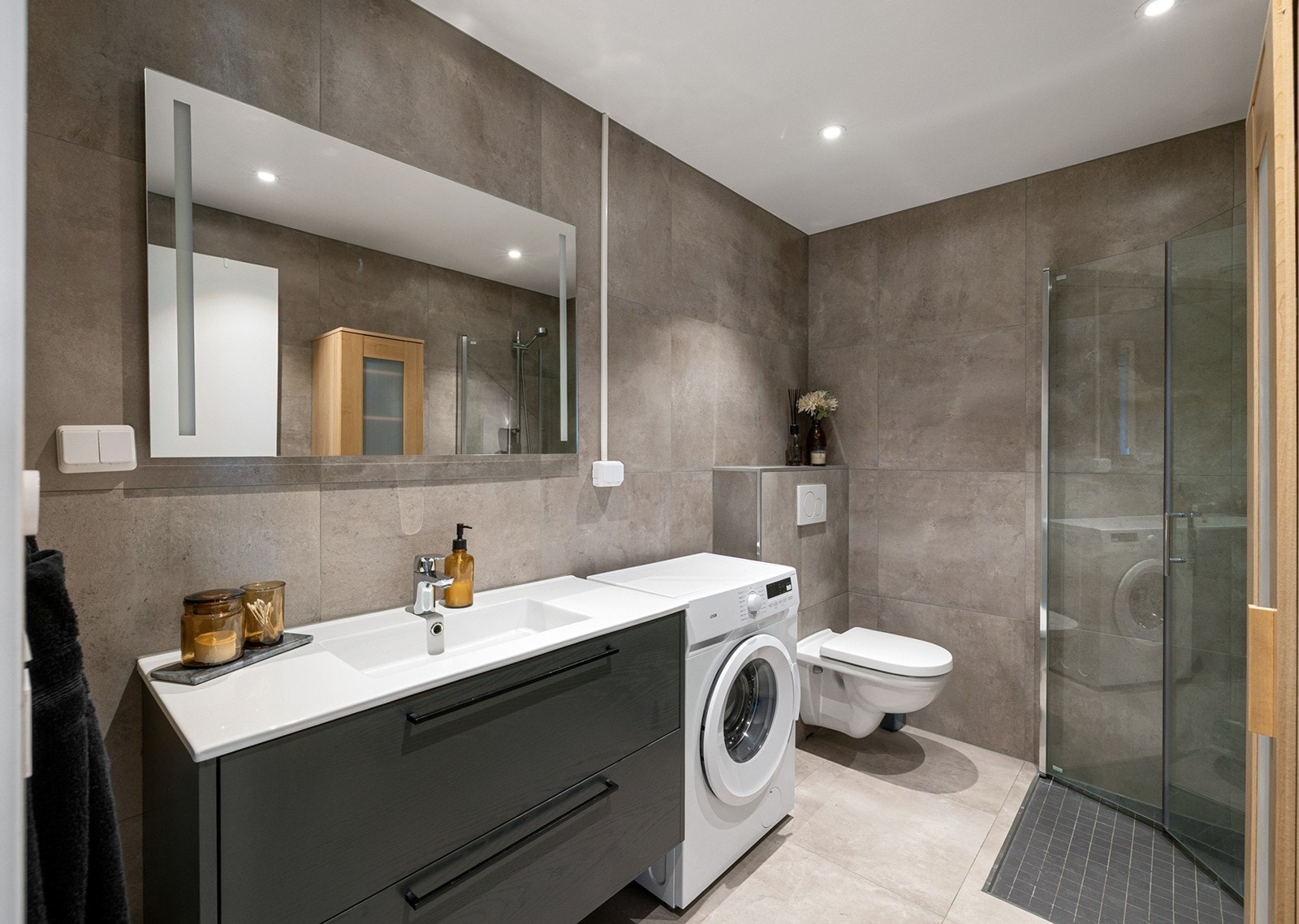 Delikat og romslig bad med flislagt gulv med gulvvarme og flislagte vegger. Badet er innredet med servant med underskap, speil med belysning. Videre er det en dusjsone med glassvegger, noe som gir en praktisk og stilren løsning. Galleribilde