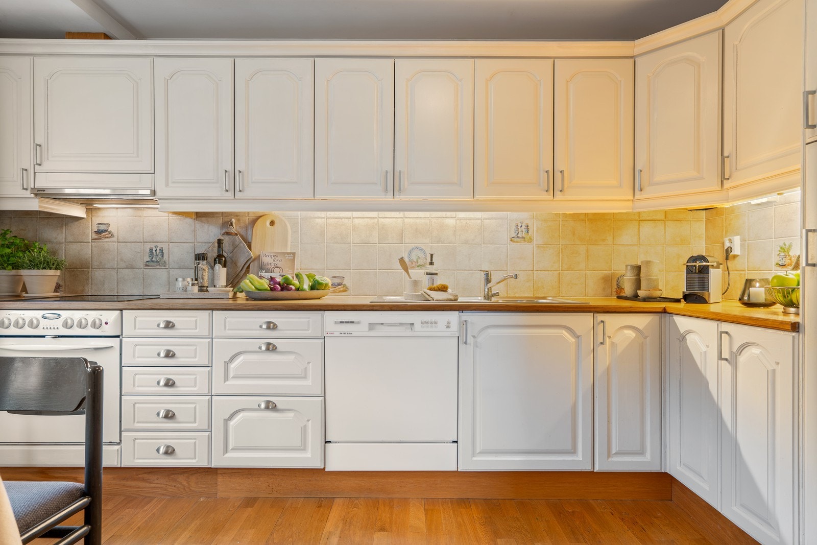 Kjøkkenet er utstyrt med kjøleskap, oppvaskmaskin, platetopp og stekeovn, som alle medfølger i handelen. Fliser over benkeplaten gir et praktisk og stilrent uttrykk Galleribilde