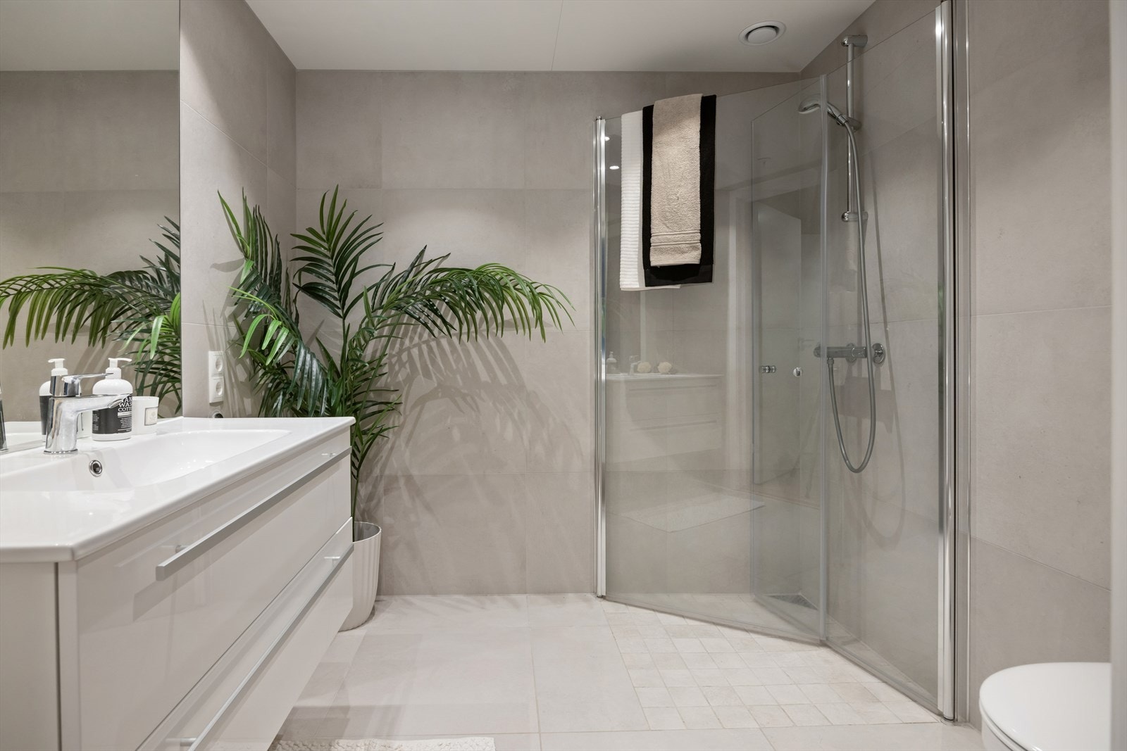 Delikat, flislagt bad fra 2025 med vegghengt toalett og dusjhjørne med innfellbare glassvegger. Galleribilde