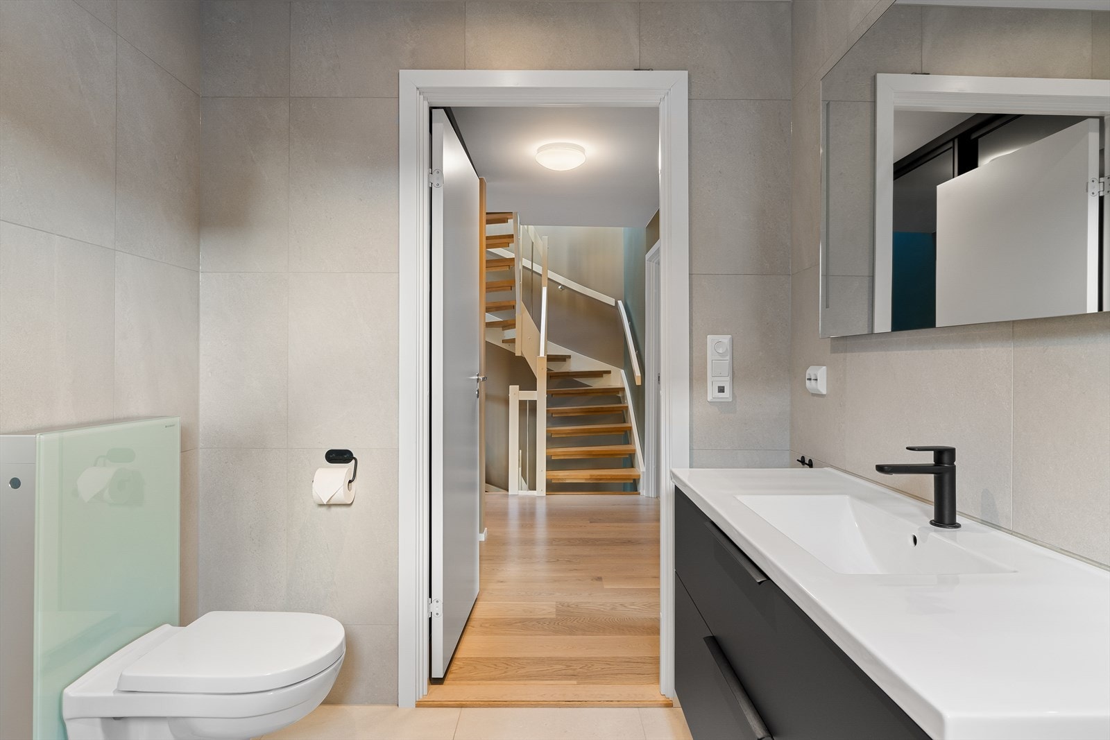 Stilrent baderom med helflisede overflater, dusjhørne, servant med innredning, speil med belysning og vegghengt toalett. Galleribilde