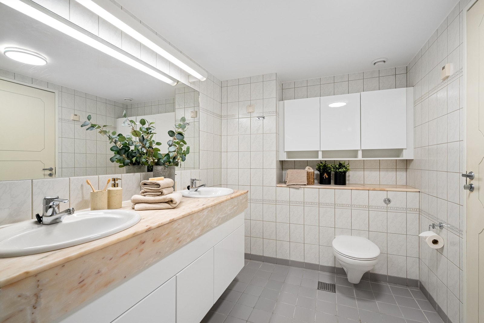 Det er varmekabler i gulv, servant med marmor, stort speil på vegg. Ekstra oppbevaring i skap på vegg. Galleribilde
