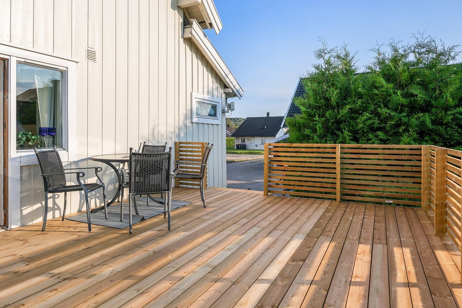 En nybygd veranda med tregulv og sittegruppe - et flott sted å nyte morgenkaffen, samle venner til grilling eller bare slappe av på varme sommerdager. Galleribilde