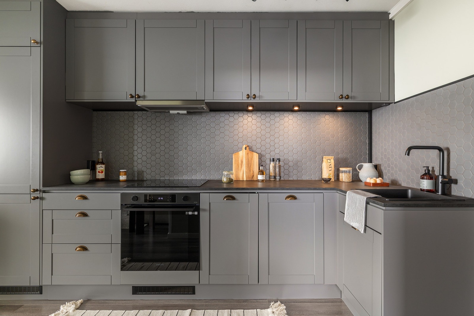 Kjøkkeninnredning med profilerte fronter. Benkeplater av laminat. Nedfelt oppvaskkum i kompositt med ettgreps armatur. Pene fliser mellom kjøkkenbenk og overskap. Benkskapsbelysning og stikkontakter. Galleribilde