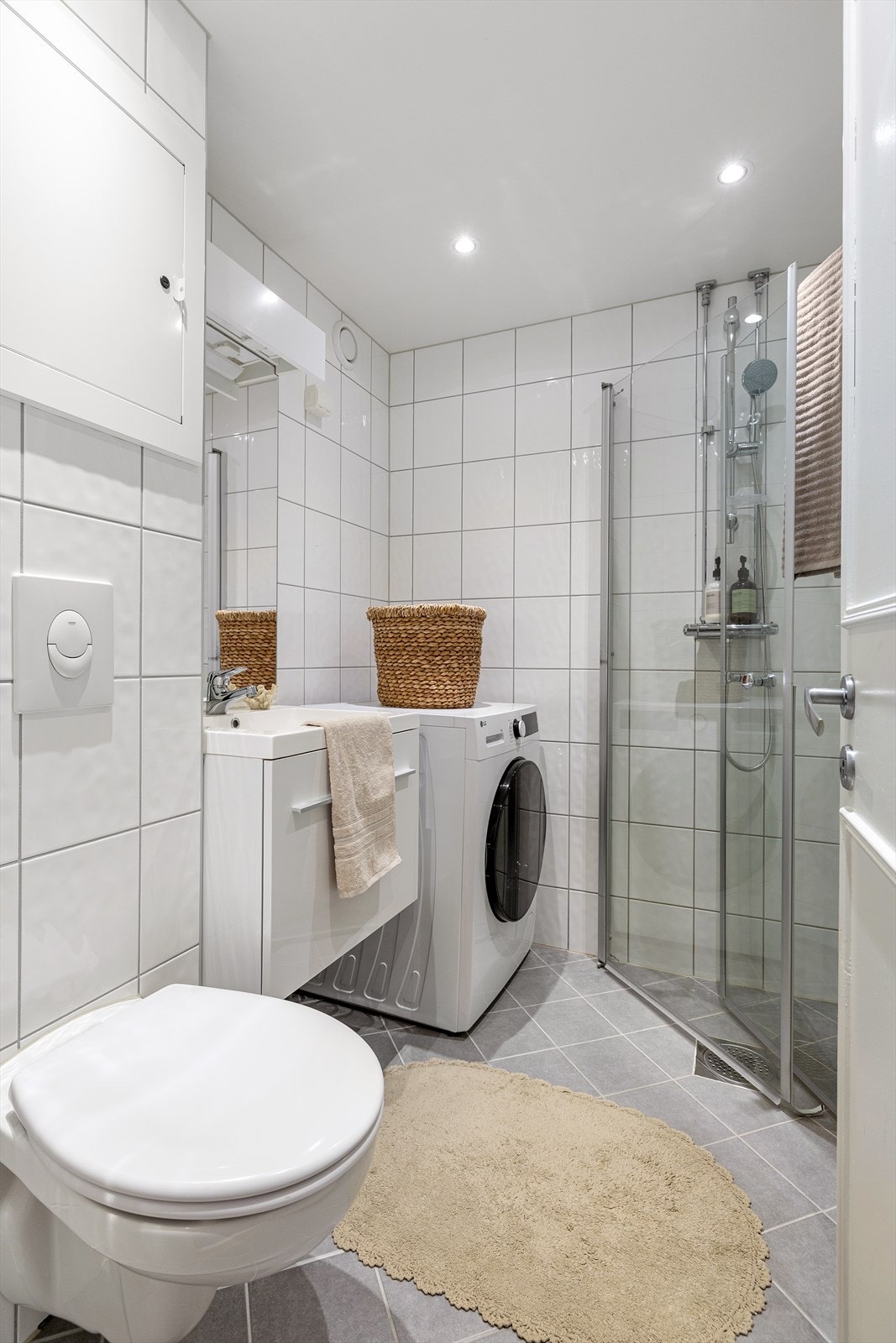 Badet inneholder vegghengt servantskap, speil med belysning, gulvstående høyskap, dusj med innfellbare glassdører og vegghengt toalett. Galleribilde