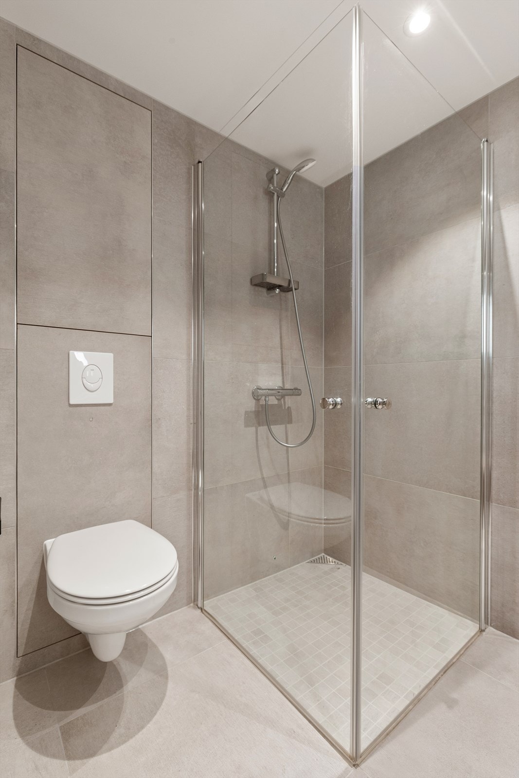 Badet er utstyrt med heldekkende servant med underskap, speil med lys, dusjhjørne med glassdører og vegghengt toalett Galleribilde