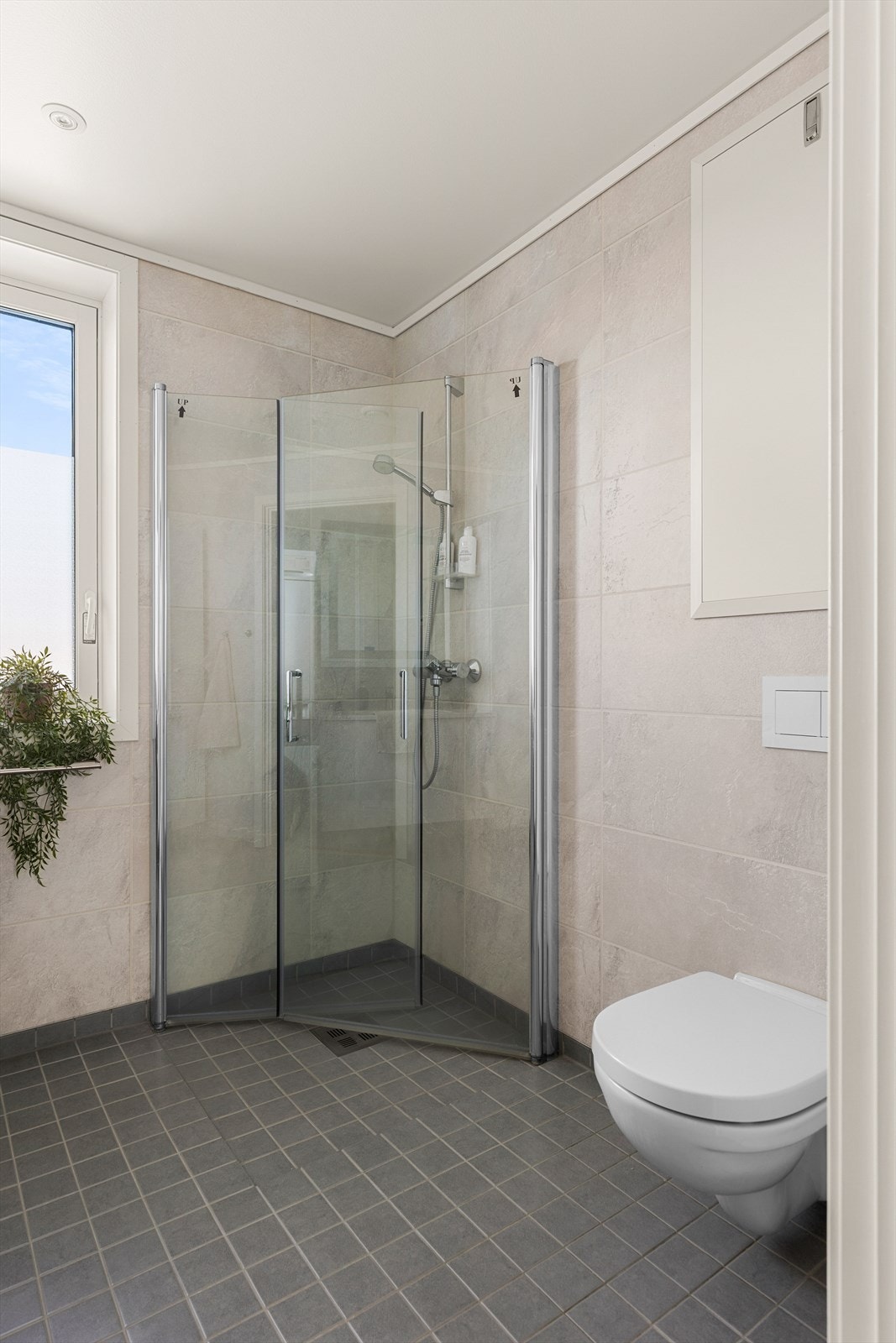 Badet er innredet med dusjkabinett av glass, veggmontert toalett, innredning med servant og opplegg for vaskemaskin. Galleribilde
