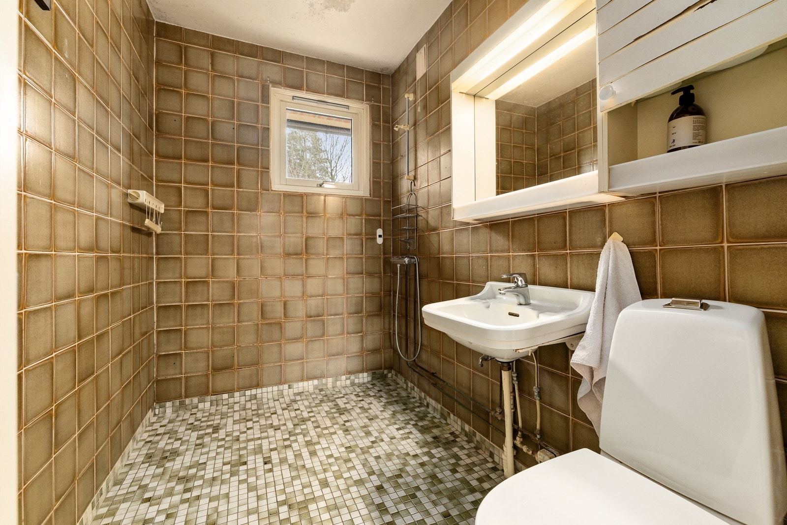 Flislagt gulv med gulvvarme. Flislagte vegger. Malte flater i himling. Vegghengt servant med armatur. Speil med overlys. Dusjhjørne. Vegghengt dusjarmatur. Galleribilde