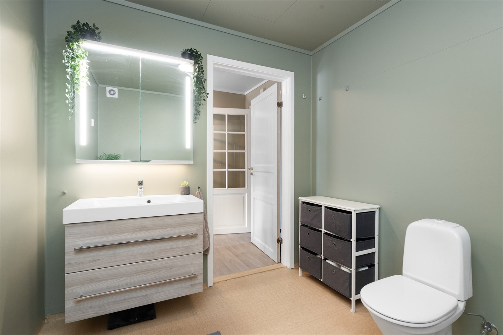 Bad med belegg på gulv og våtromstapet på vegger. Her er det innredningen av nyere dato med heldekkende hvit vask, underskuffer med slette fronter og overskap med speildører og lys. Galleribilde