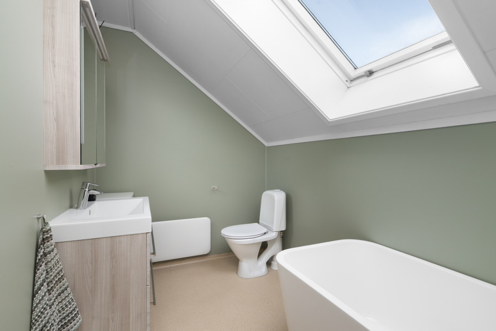 Bad med belegg på gulv og våtromstapet på vegger. Her er det innredningen av nyere dato med heldekkende hvit vask, underskuffer med slette fronter og overskap med speildører og lys. Badet har også toalett og badekar. Naturlig ventilering. Galleribilde