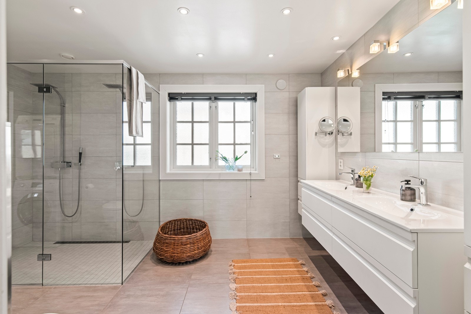 Baderomsinnredningen imponerer med hvite fronter og inkluderer en heldekkende dobbelservant på en elegant skuffeseksjon, to høyskap og et stort speil med innebygd belysning. Galleribilde