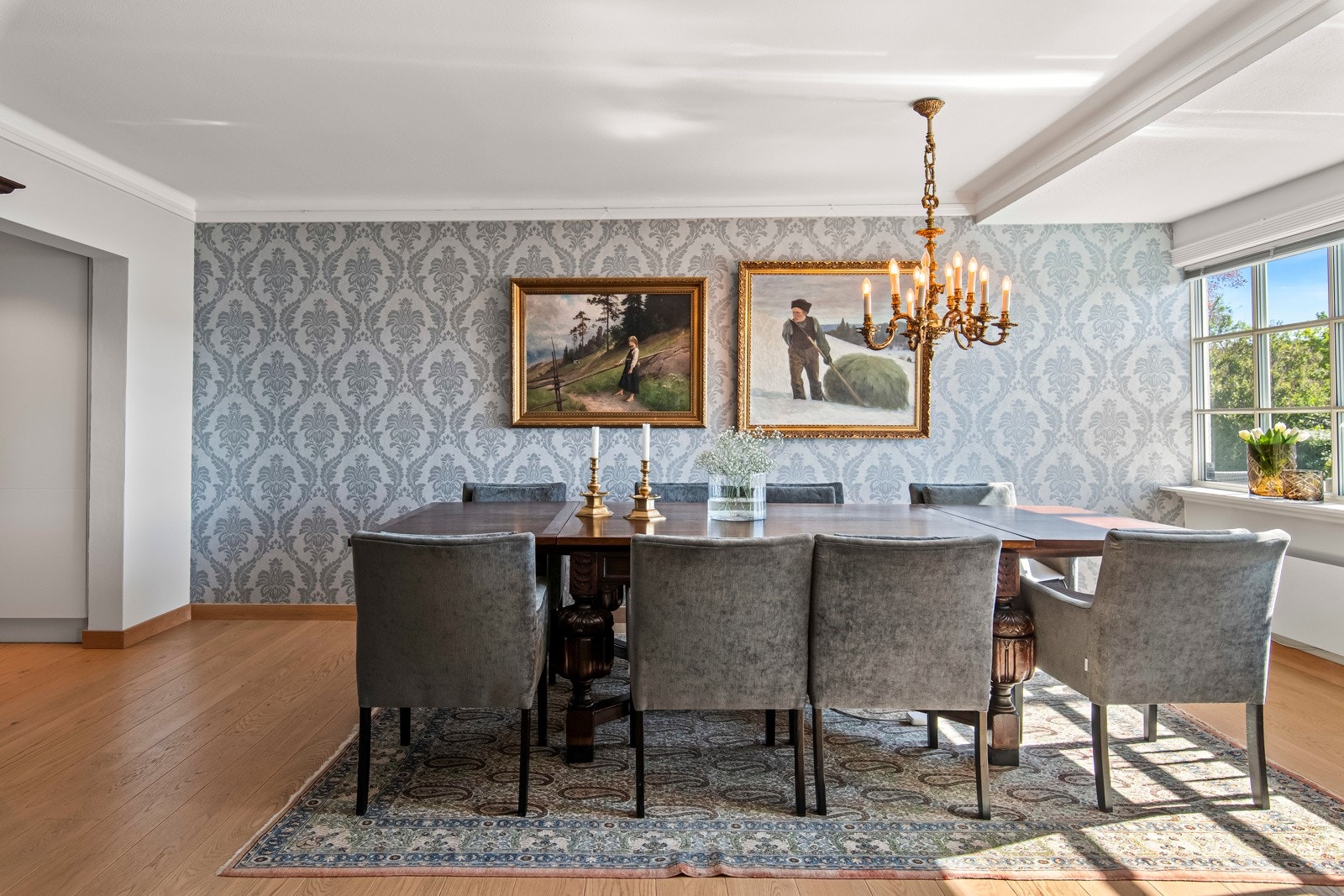 De lyse grå veggene komplementerer det gylne parkettgulvet, mens en vegg i spisestuen er kledd med en klassisk, mønstret tapet som gir en sofistikert touch. Galleribilde