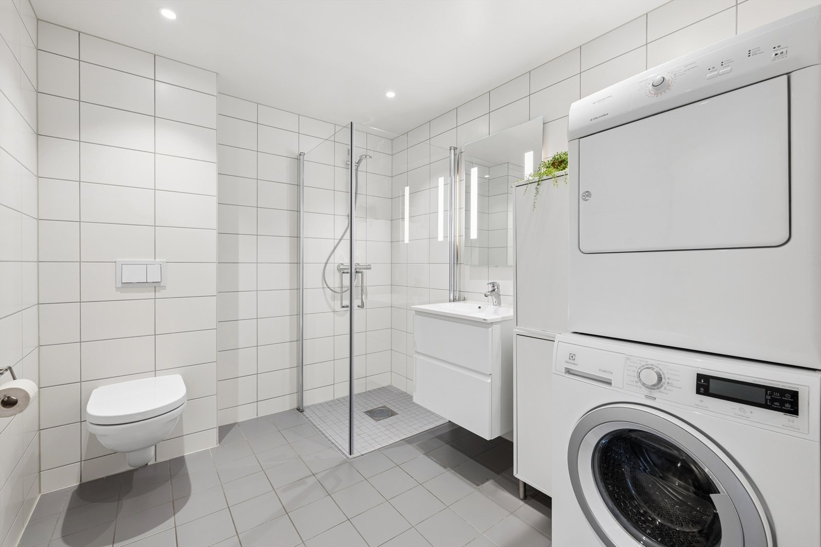 Badet er innredet med baderomsmøbel med hvite fronter, servant og speil med belysning. Galleribilde