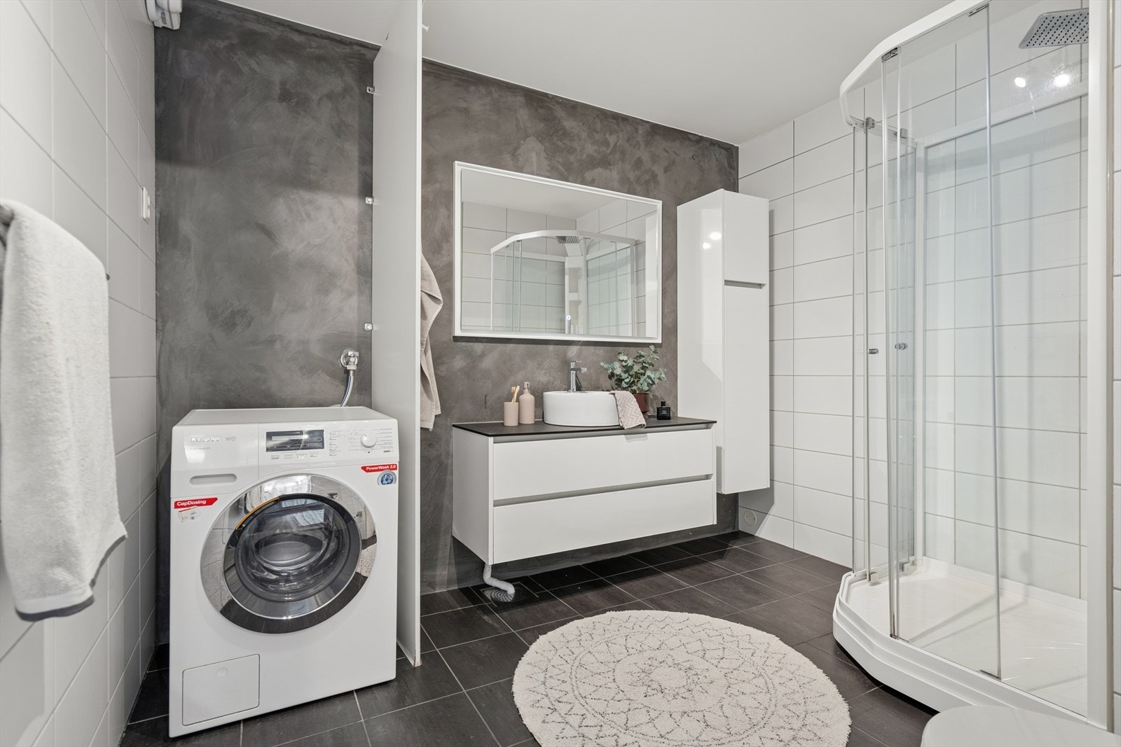 Badet i hoveddelen er flislagt og utstyrt med speil, servant med seksjon, høyskap, vegghengt toalett, dusjkabinett og opplegg for vaskemaskin. Galleribilde