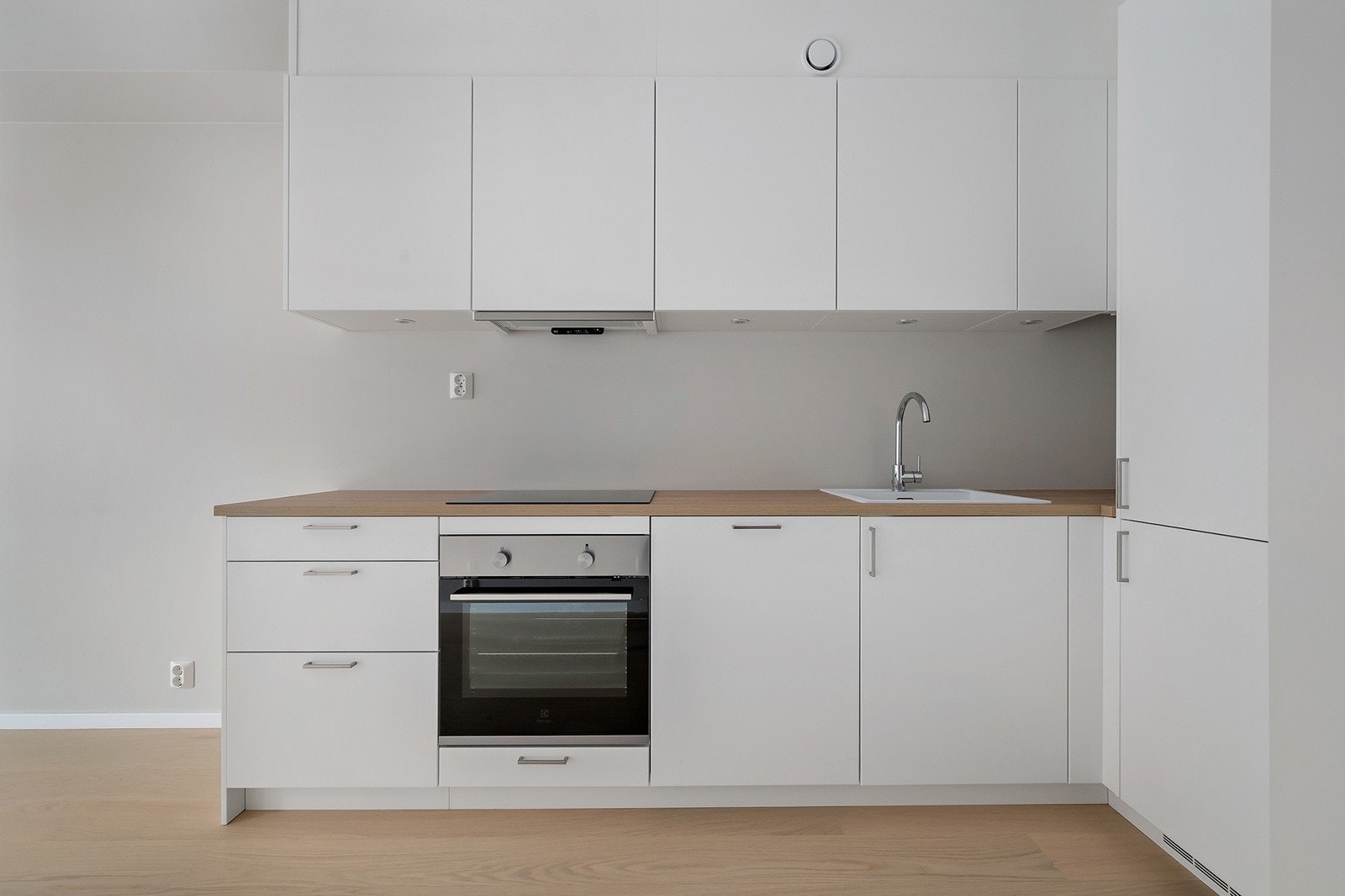 Kjøkkenet er innredet med glatte fronter, integrerte hvitevarer og benkeplate av laminat med enkel kum i kompositt. Galleribilde