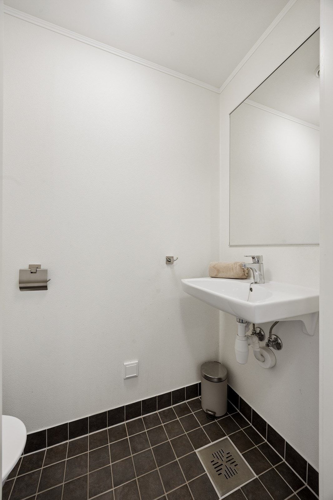 Praktisk toalettrom ved entréen med gulvstående toalett, servant med ettgreps kran og speil på vegg over servant. Galleribilde