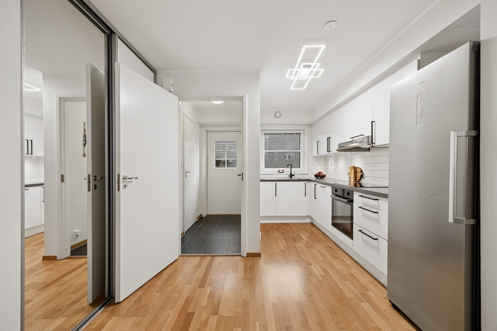 Kjøkkenet er lyst og moderne med glatte, hvite fronter og en laminatbenkeplate med nedfelt stålkum. Galleribilde