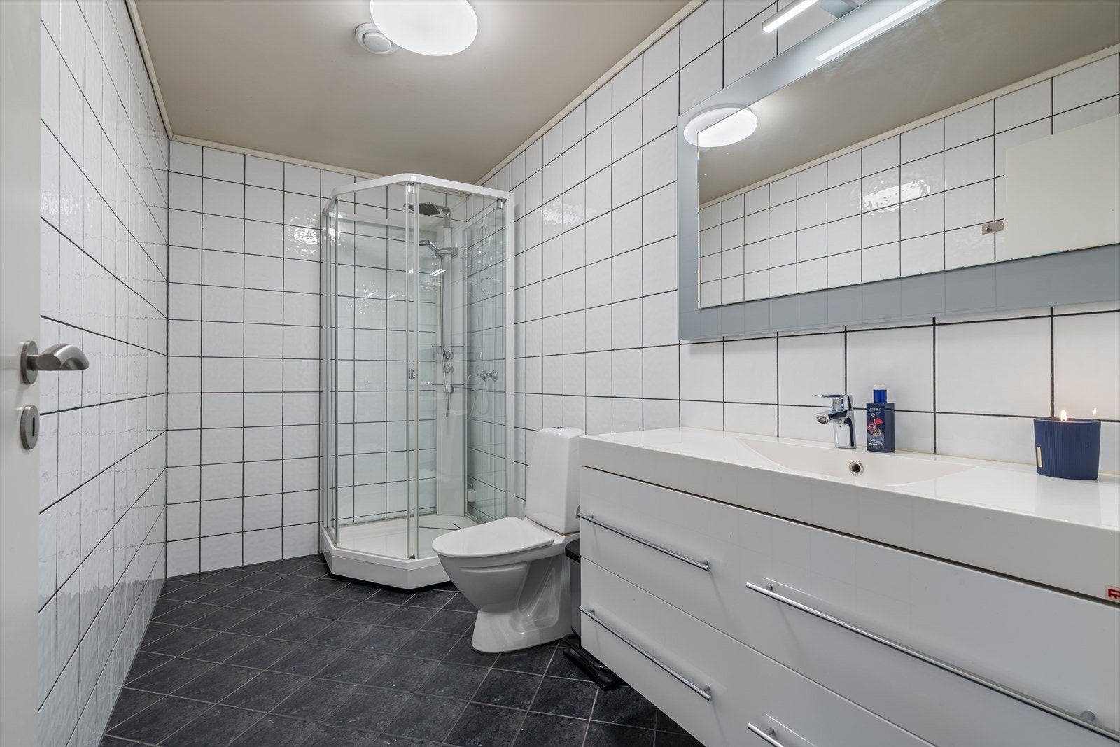 Baderommet er lyst og tidsriktig innredet med fliser på både gulv- og veggoverflater. Badet er innredet med wc, vask i seksjon og dusjkabinett. met er lyst og tidsriktig innredet Galleribilde