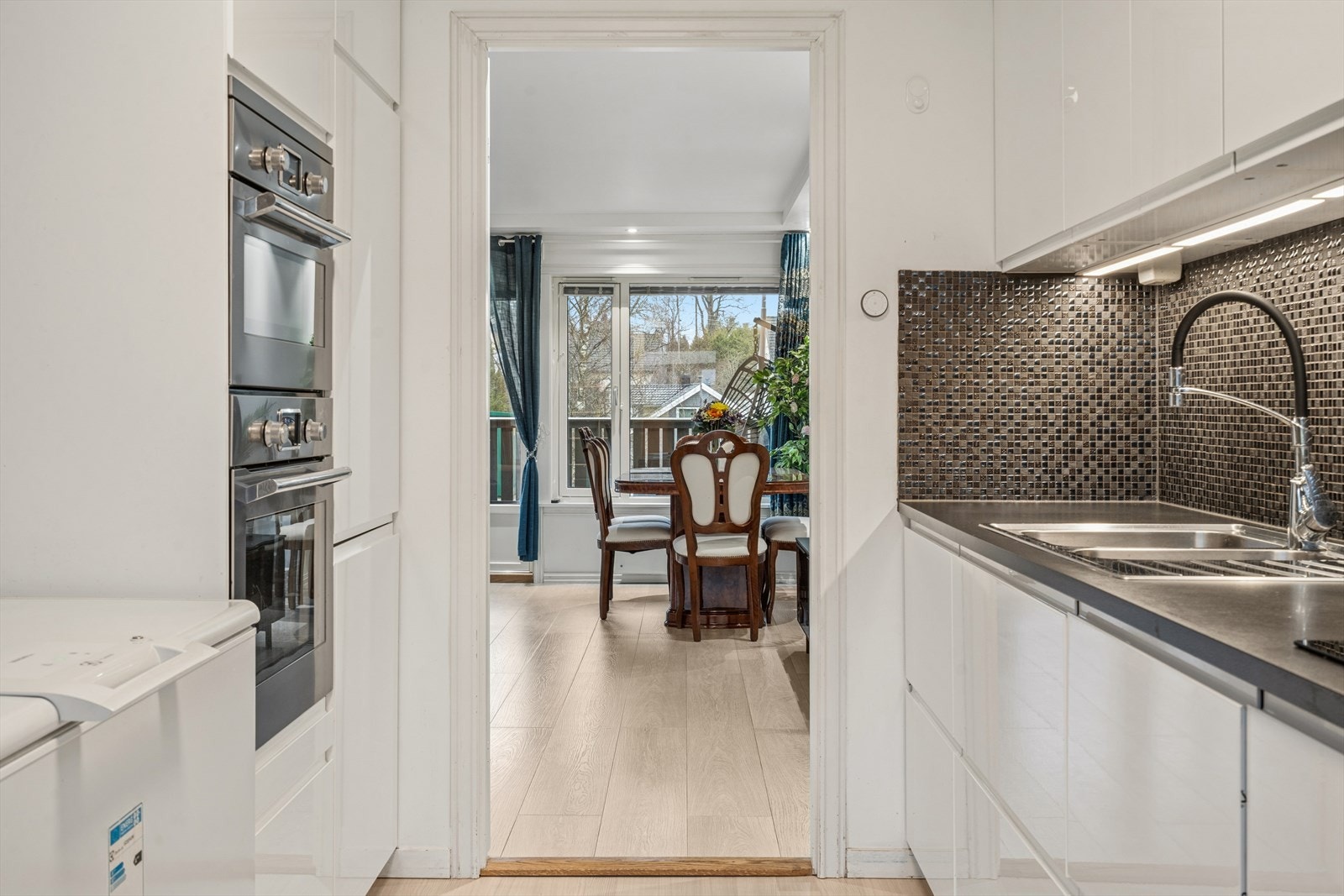 Kjøkkenet er pent innredet med hvite, glatte fronter kombinert med en mørk laminatbenkeplate som gir rommet et moderne og tidsriktig uttrykk. Galleribilde