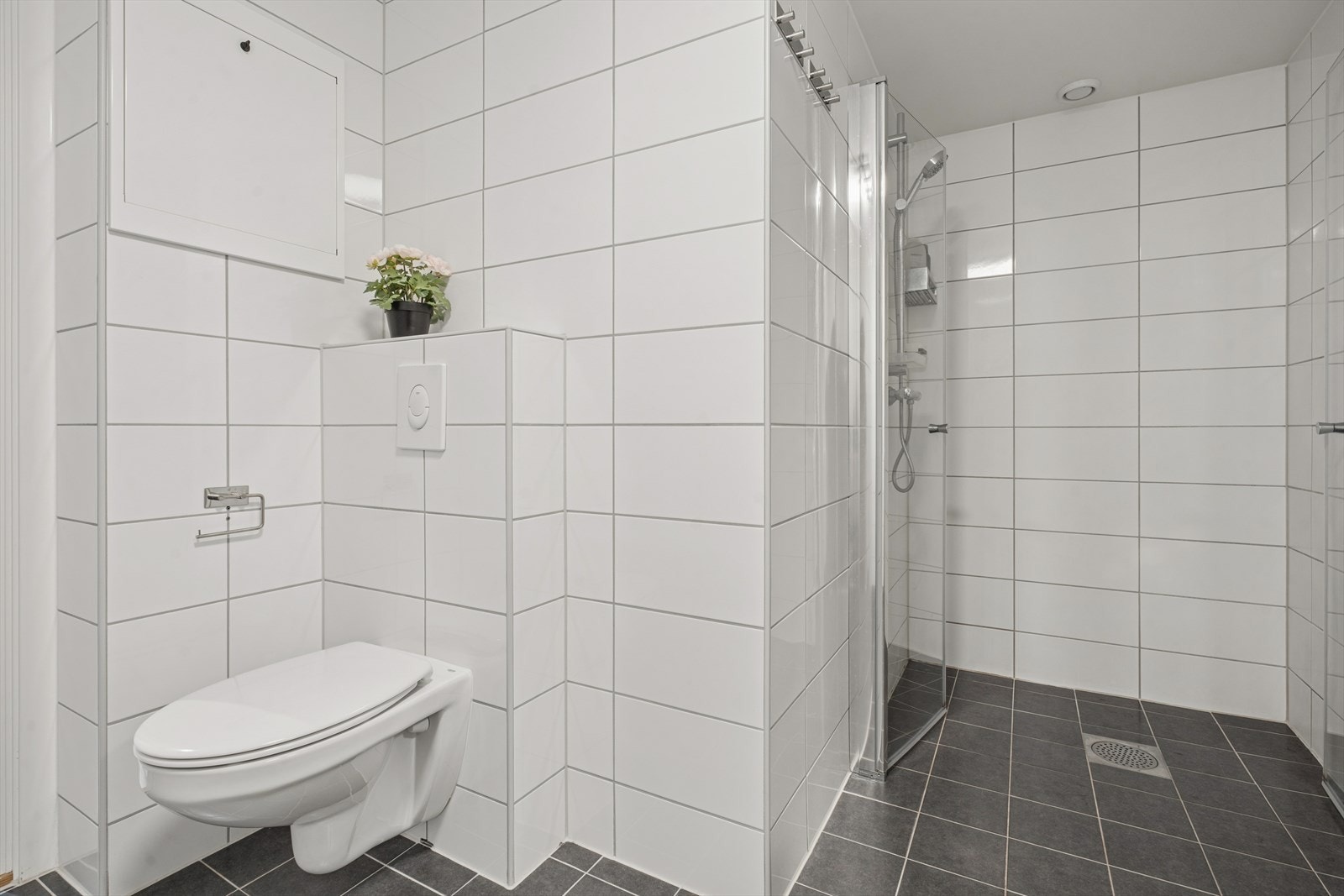 Innredningen består av nedfelt servant med praktisk underskap, veggmontert toalett og et moderne dusjhjørne med dusjvegger. Galleribilde