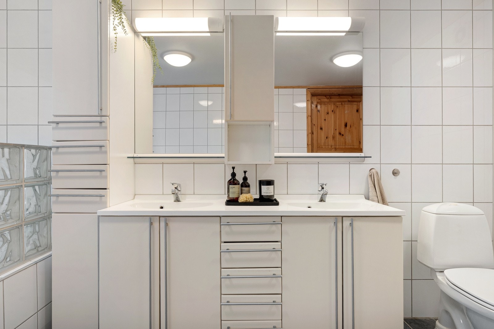 Lys baderomsinnredning med dobbel servant, skap og speil med overlys.