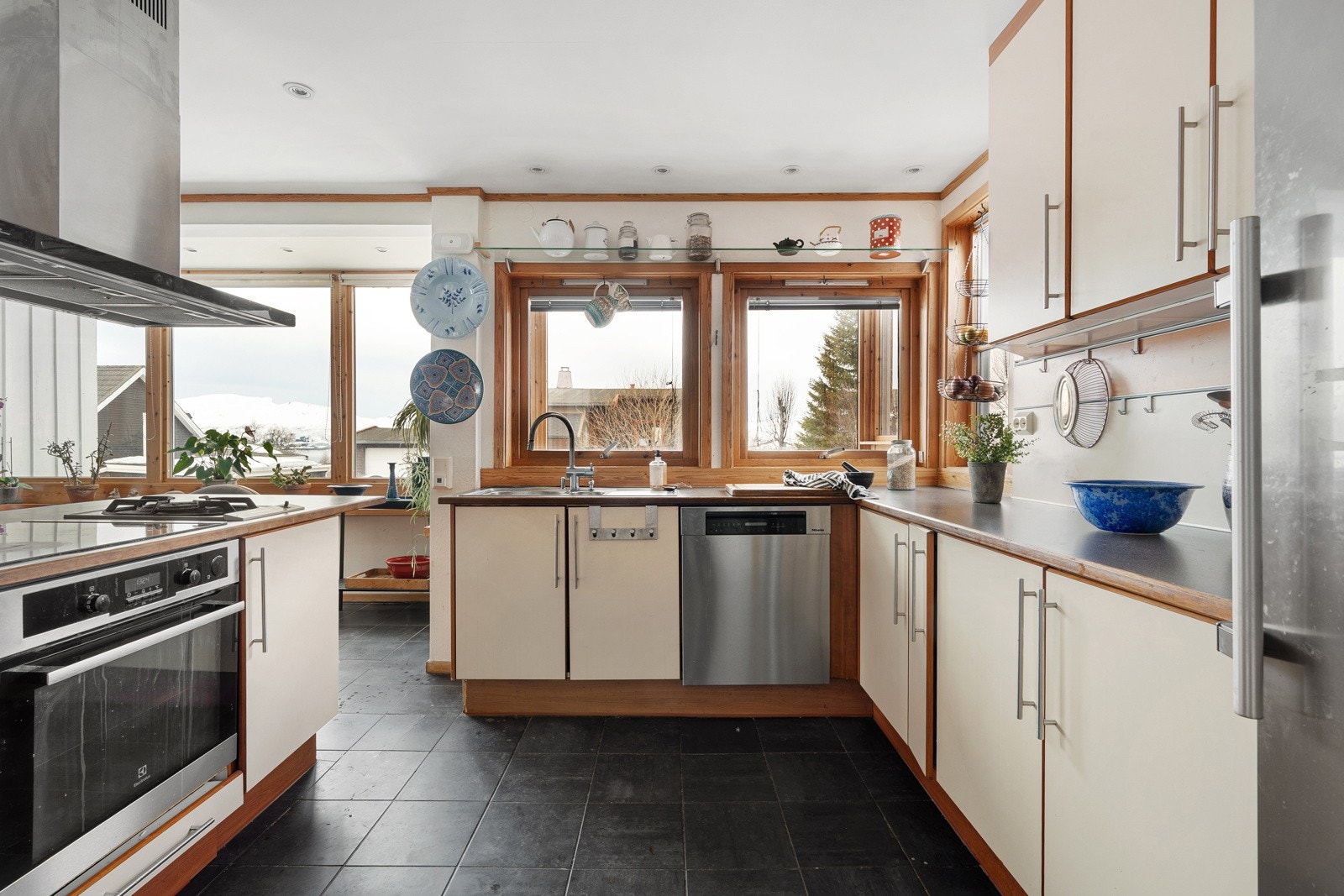 Kjøkkeninnredning med takhøye overskap og lyse slette fronter. Fliser på gulv og gulvvarme.