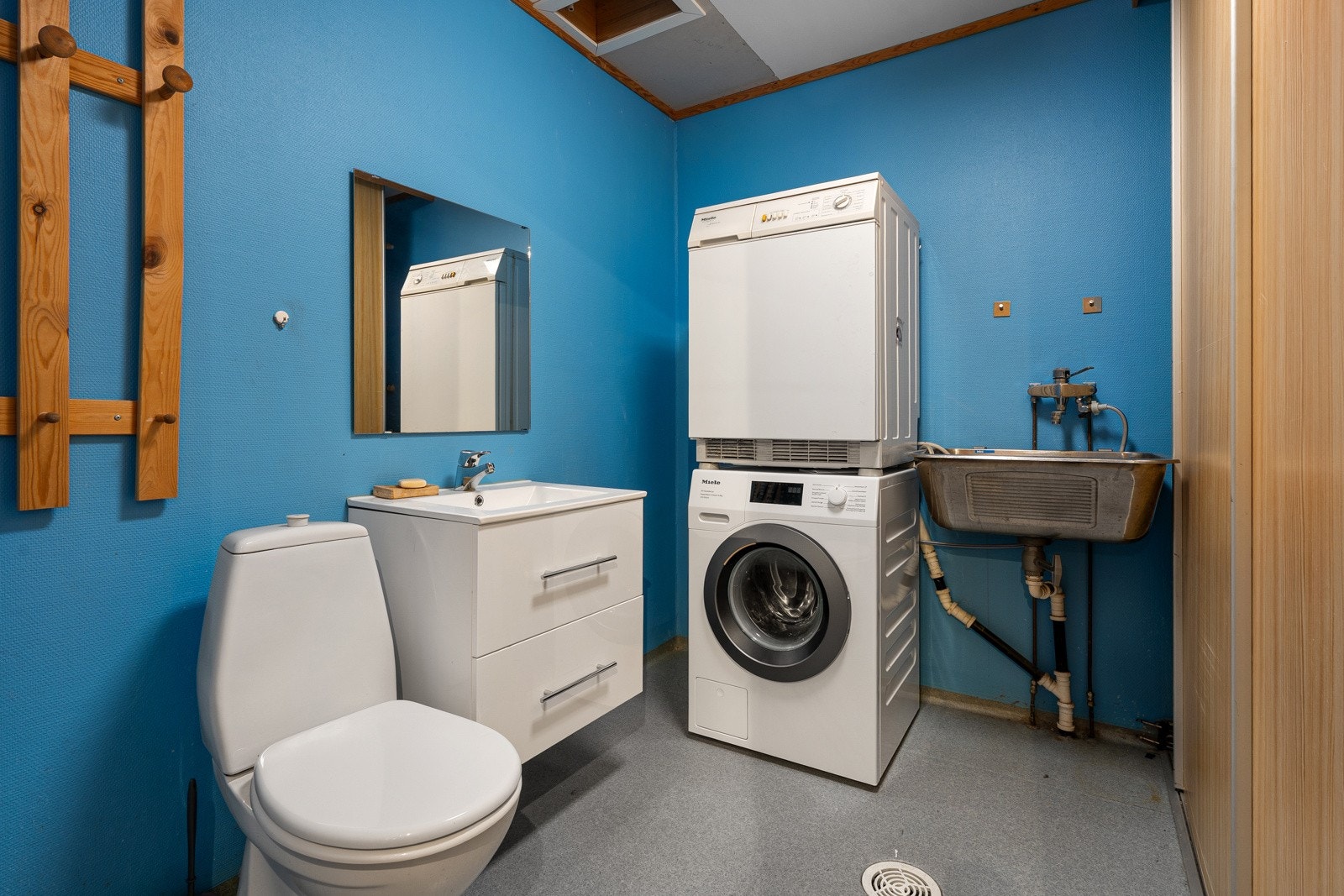 Vaskerom/wc i første plan med wc, baderomsinnredning med servant, garderobeskap og opplegg for vaskemaskin