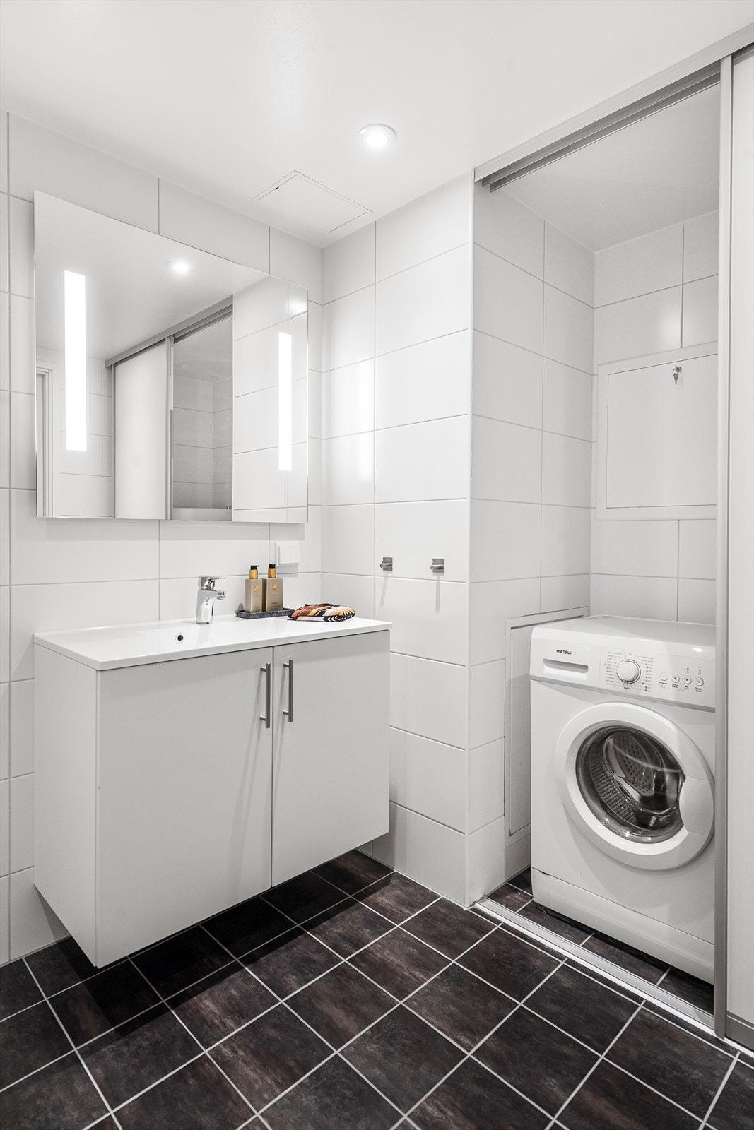 Badet fungerer også som vaskerom med opplegg til vaskemaskin i nisje med skyvedør. Galleribilde