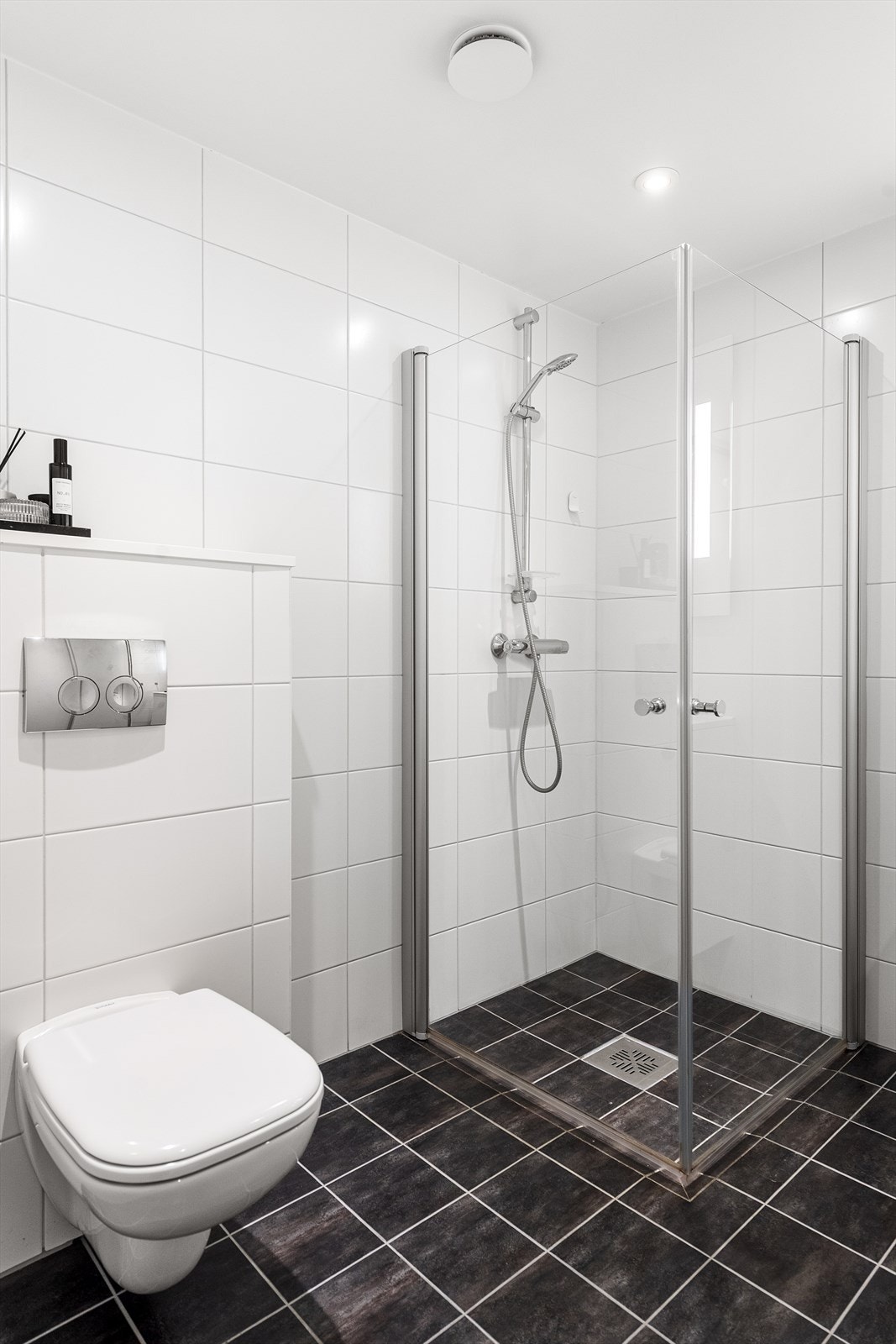 Badet er innredet med vegghengt toalett, dusjhjørne med innfellbare glassdører og baderomsinnredning. Galleribilde