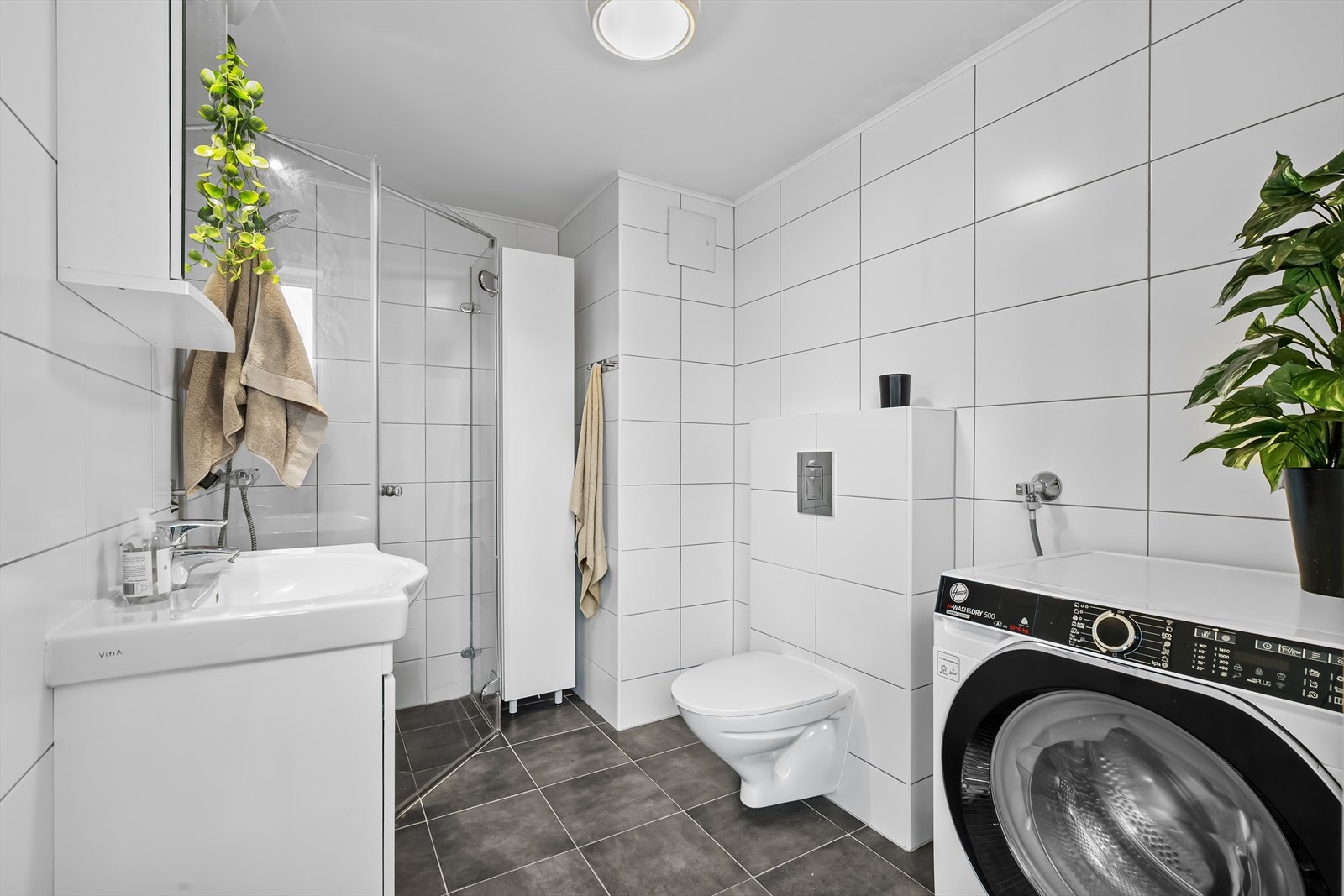 Badet er innredet med vegghengt toalett, dusjnisje med to skjermvegger og dør, samt baderomsinnredning med servantskap og hel, nedfelt servant. Galleribilde